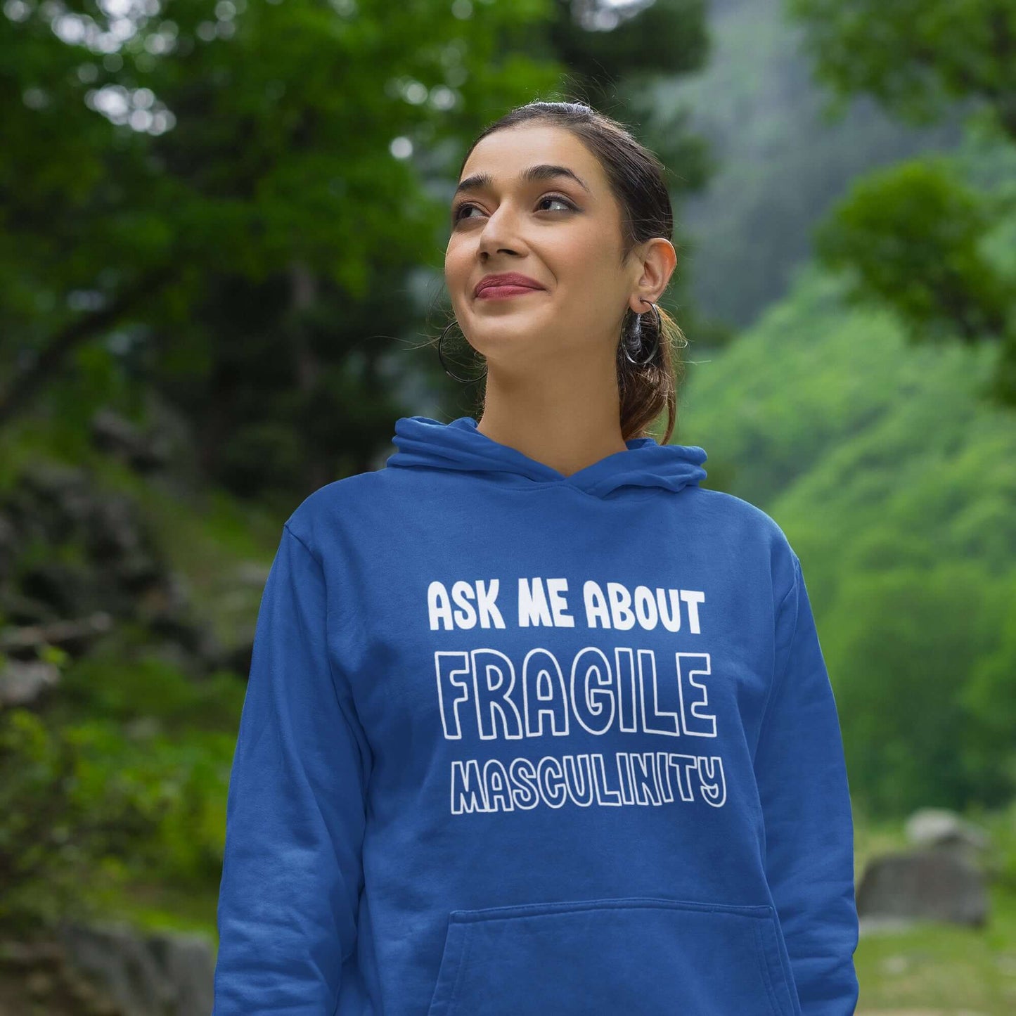 Smiling woman wearing a royal blue hoodie sweatshirt with the phrase Ask me about fragile masculinity printed on the front.