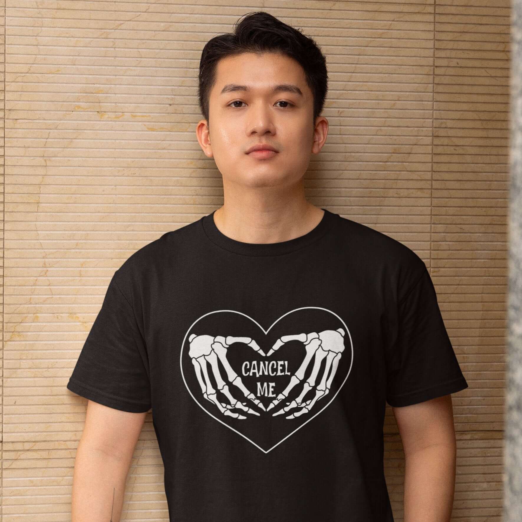 Man wearing a black t-shirt with a black heart and skeleton hands making a heart shape printed on the front. The words Cancel Me are inside of the heart.