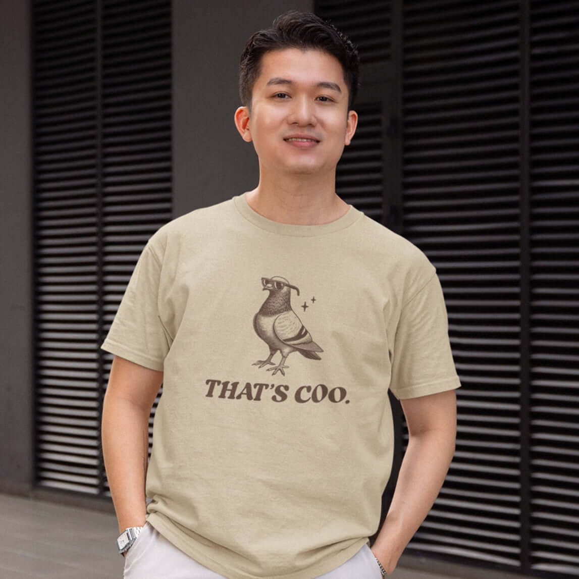 Man wearing a sand color t-shirt with an image of a pigeon and the words That's coo printed on the front.