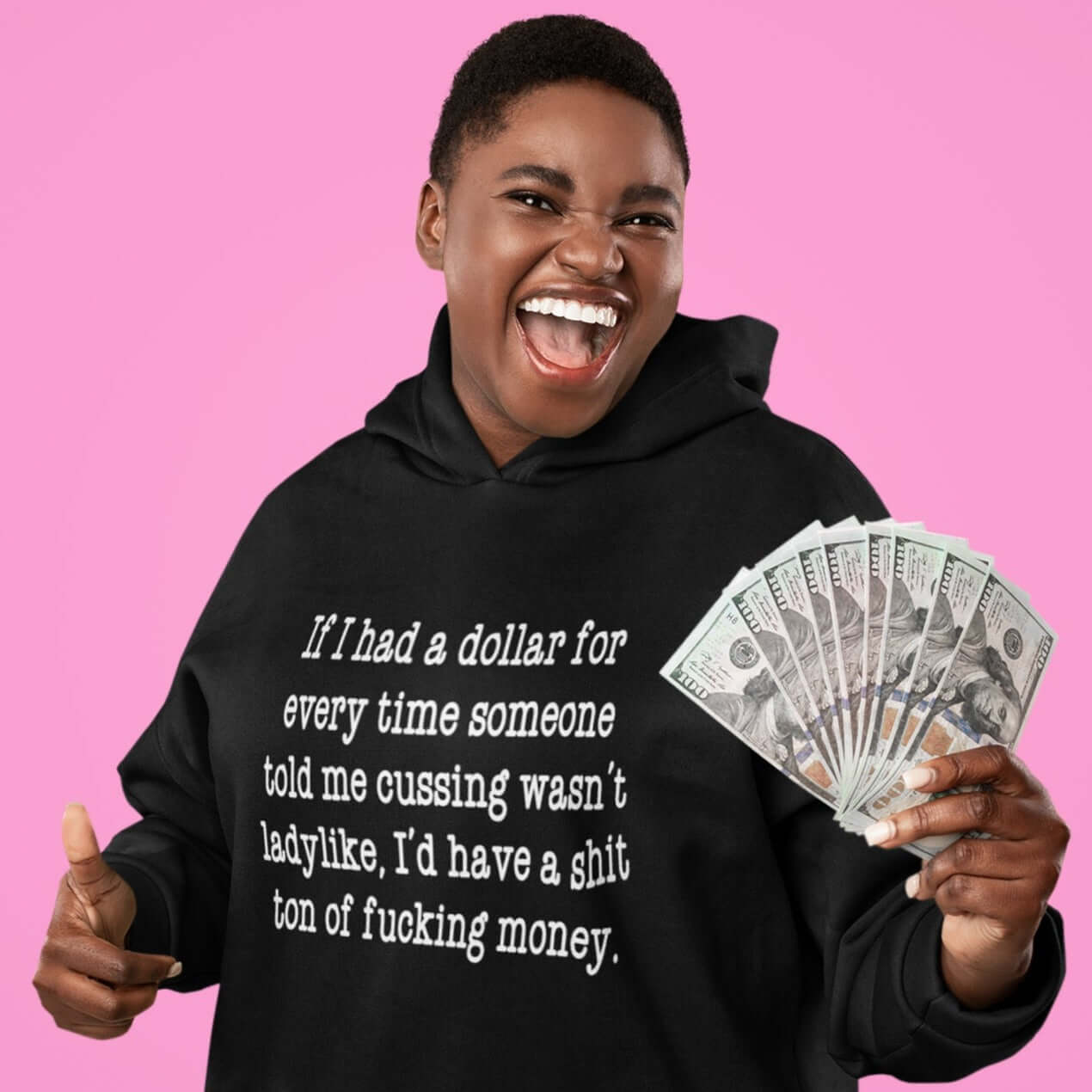 Smiling woman holding a wad of cash. She is wearing a black hoodie sweatshirt with the phrase If I had a dollar for every time someone told me cussing wasn't ladylike I'd have a shit ton of fucking money printed on the front.