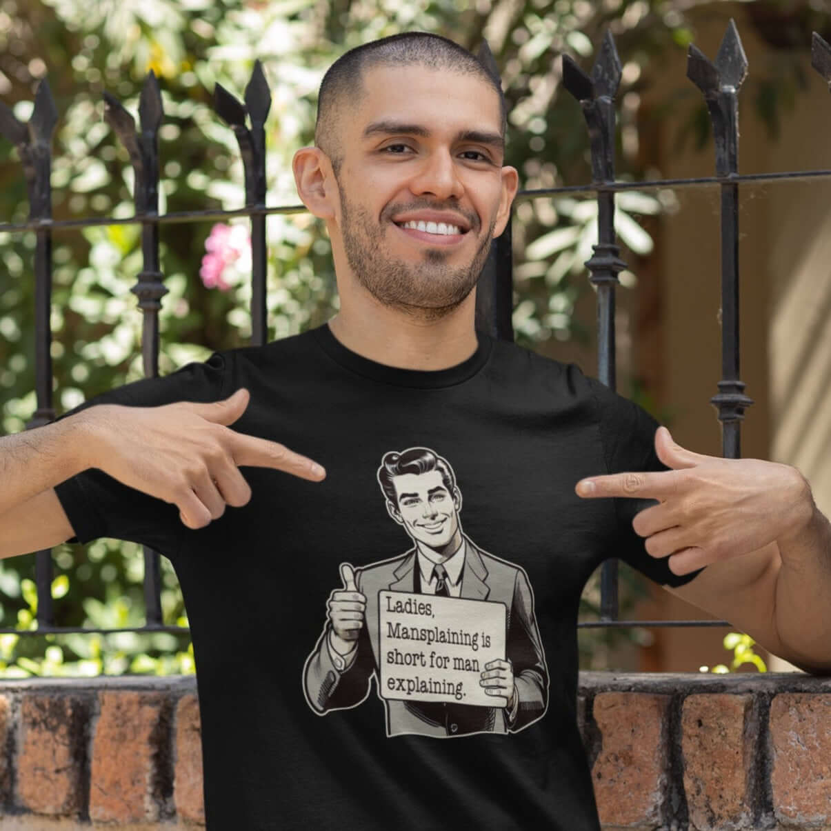 Man wearing a black t-shirt with a graphic of a retro man holding a sign. The sign says Ladies, mansplaining is short for man explaining. The graphics are printed on the front of the shirt.