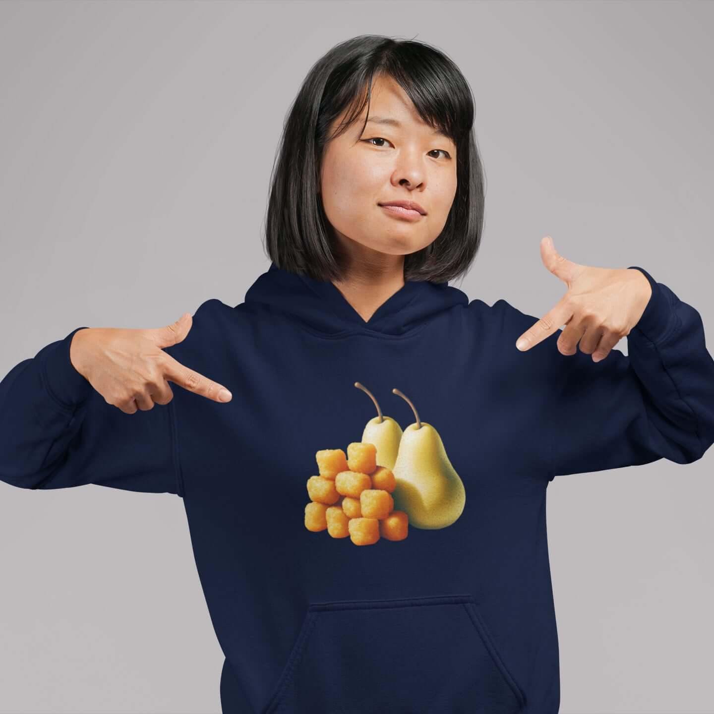 Woman wearing a navy blue hoodie with an image of tater tots and two pears printed on the front. She is pointing at the graphics on the hooded sweatshirt.