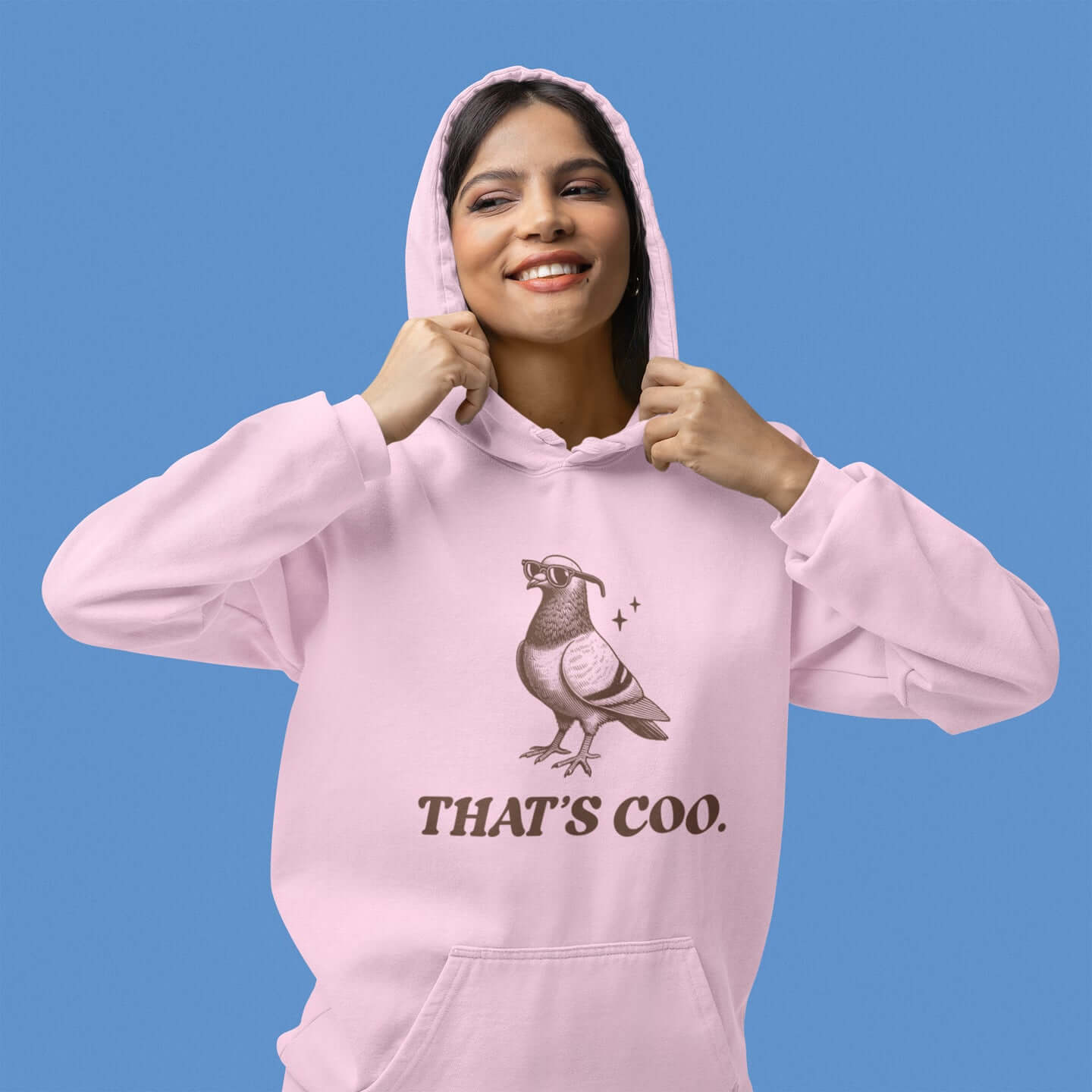 Woman wearing a light pink hoodie sweatshirt with an image of a pigeon and the words That's coo printed on the front.