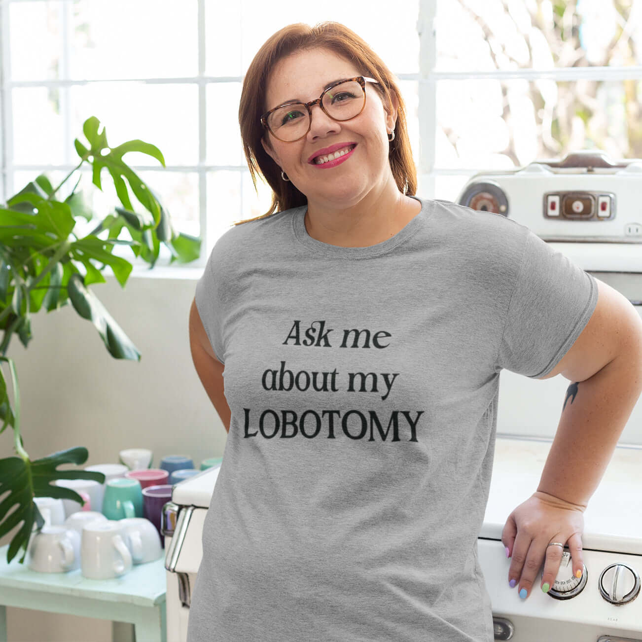 Smiling woman wearing a light grey t-shirt with the phrase Ask me about my lobotomy printed on the front.