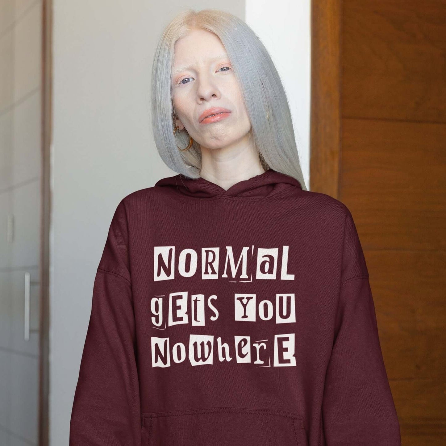 Albino woman wearing a maroon hoodie sweatshirt with the phrase Normal gets you nowhere printed on the front.