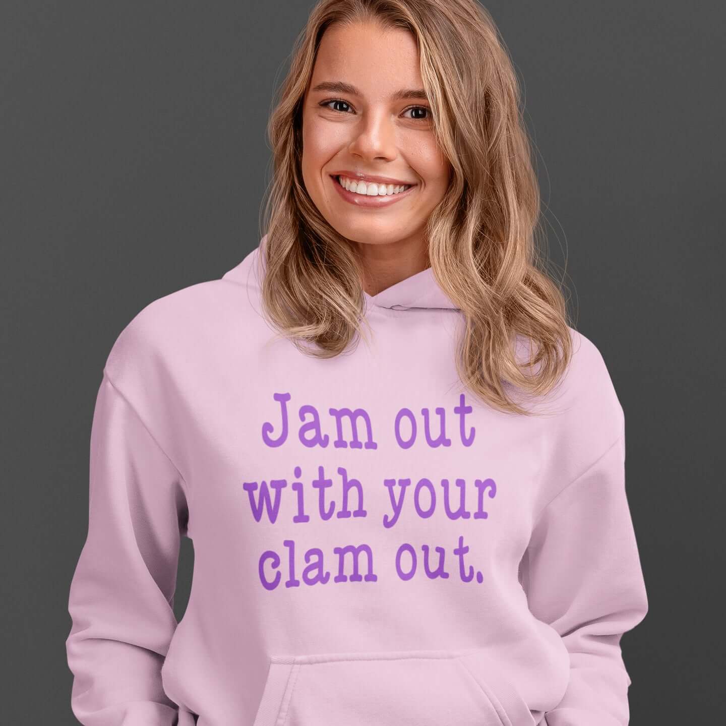 Woman wearing light pink hoodie sweatshirt with the phrase Jam out with your clam out printed on the front in purple.