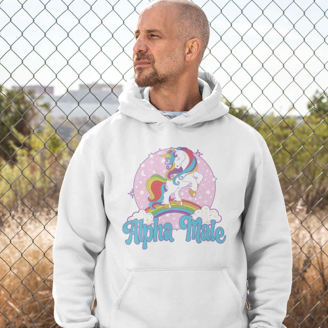 Tough looking man wearing white hoodie sweatshirt with funny pastel rainbow unicorn graphics and the words Alpha Male printed on the front.