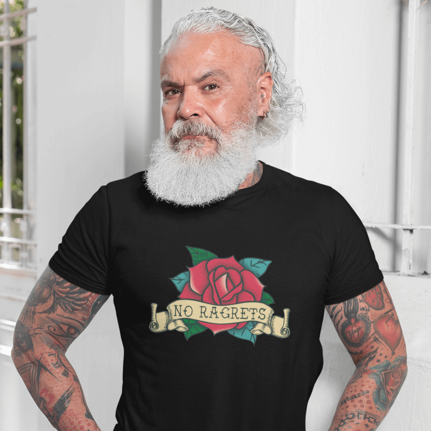 Tattooed bearded man wearing a black t-shirt with a funny image of an old school rose flash tattoo & the words no ragrets. The word regrets is intentionally misspelled.