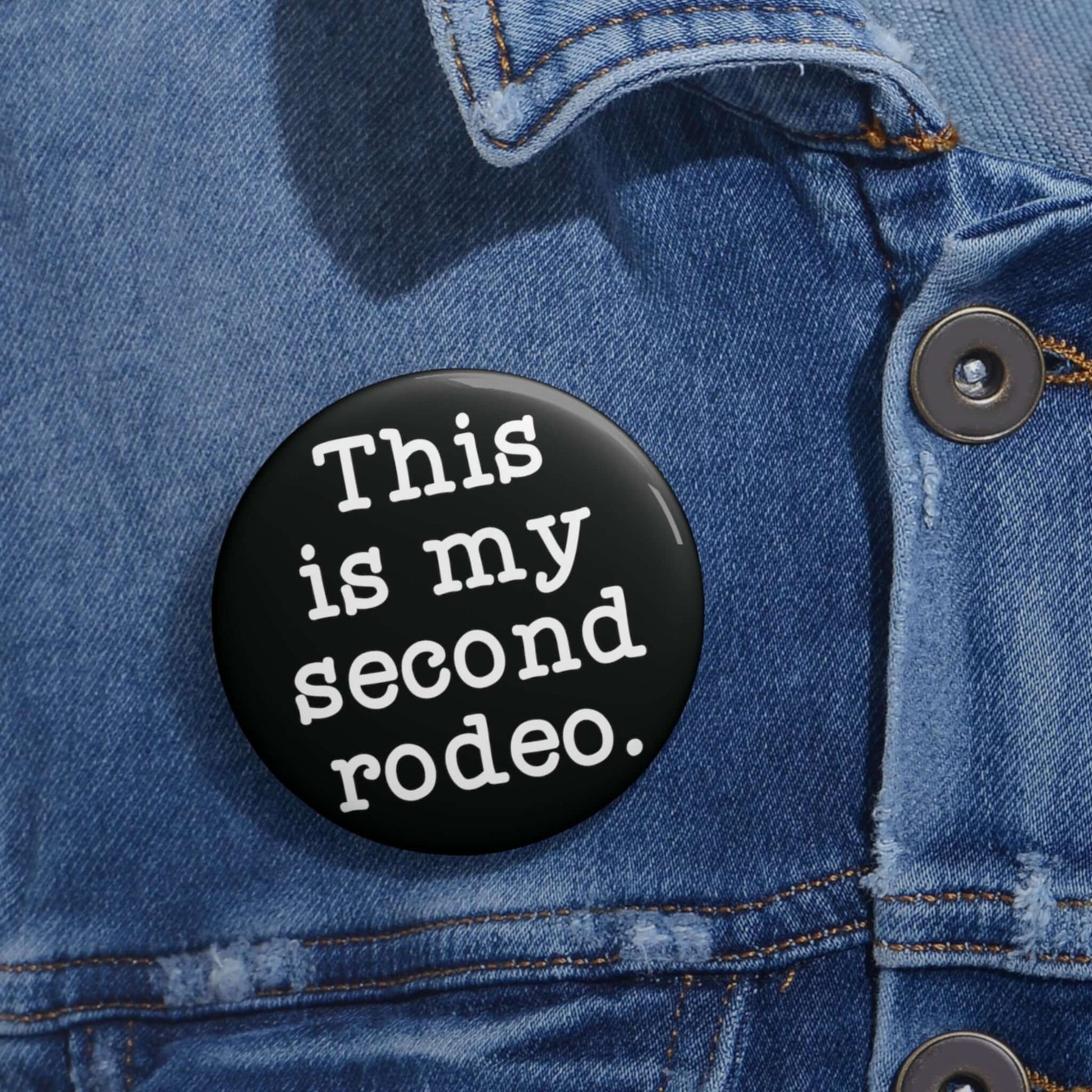 Black pin-back button with the phrase This is my second rodeo printed on it in white.