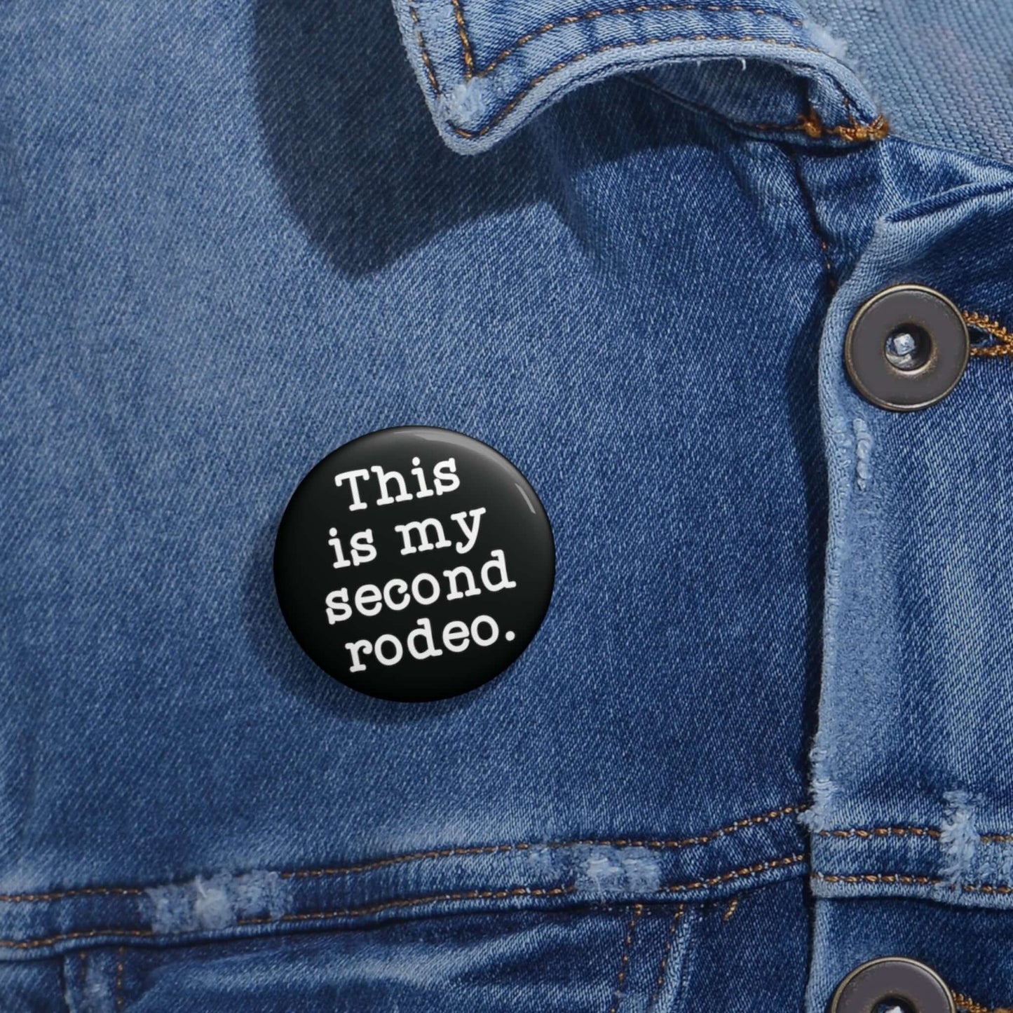 Black pin-back button with the phrase This is my second rodeo printed on it in white.