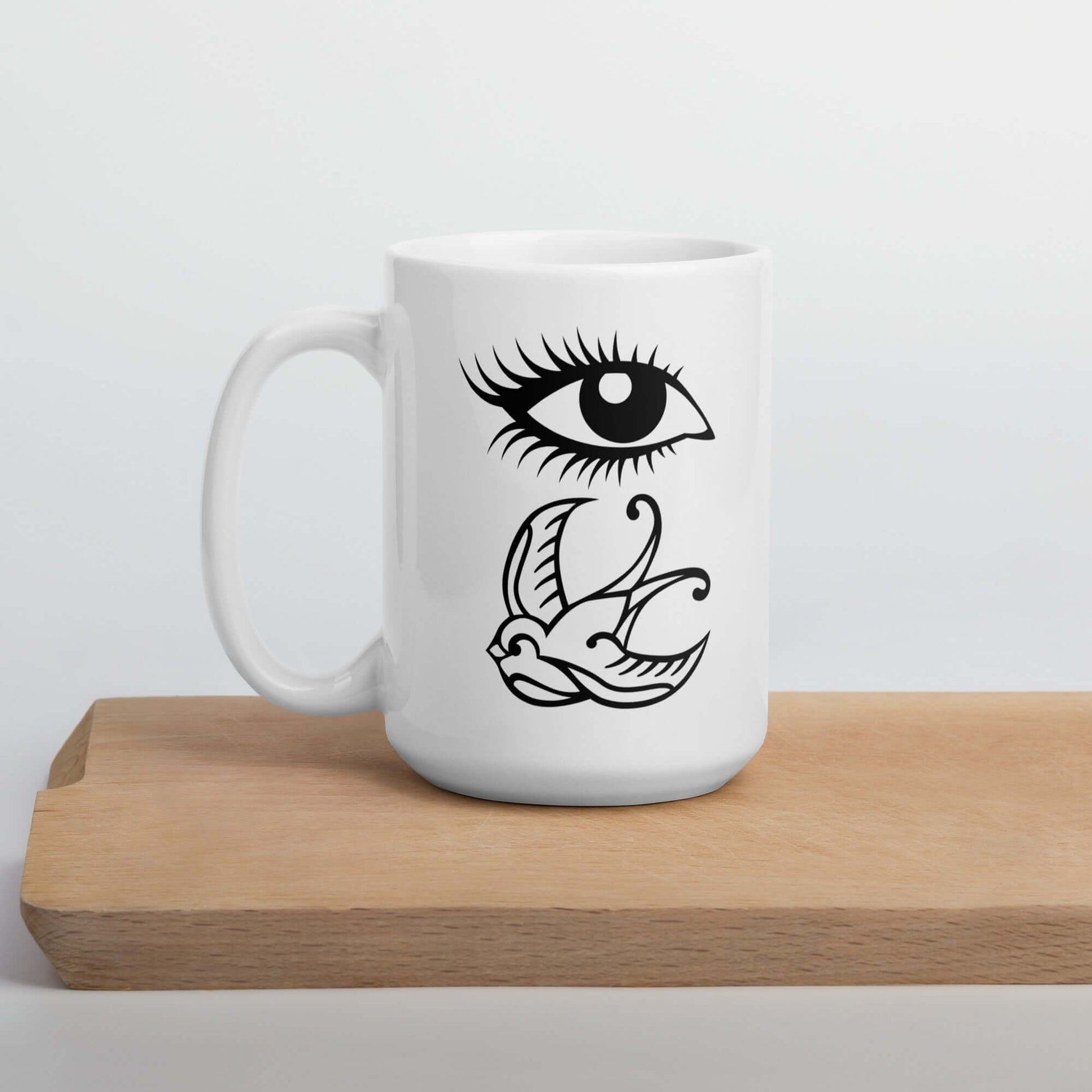 White ceramic mug with outline drawing of an eye and a swallow bird printed on both sides.