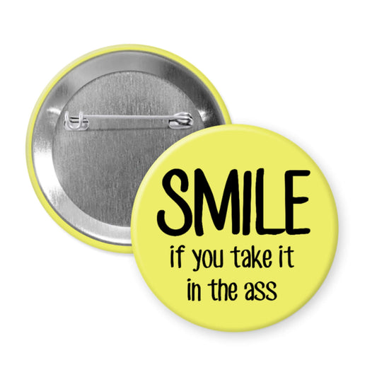 Button badge with 'SMILE if you take it in the ass' text on a yellow background