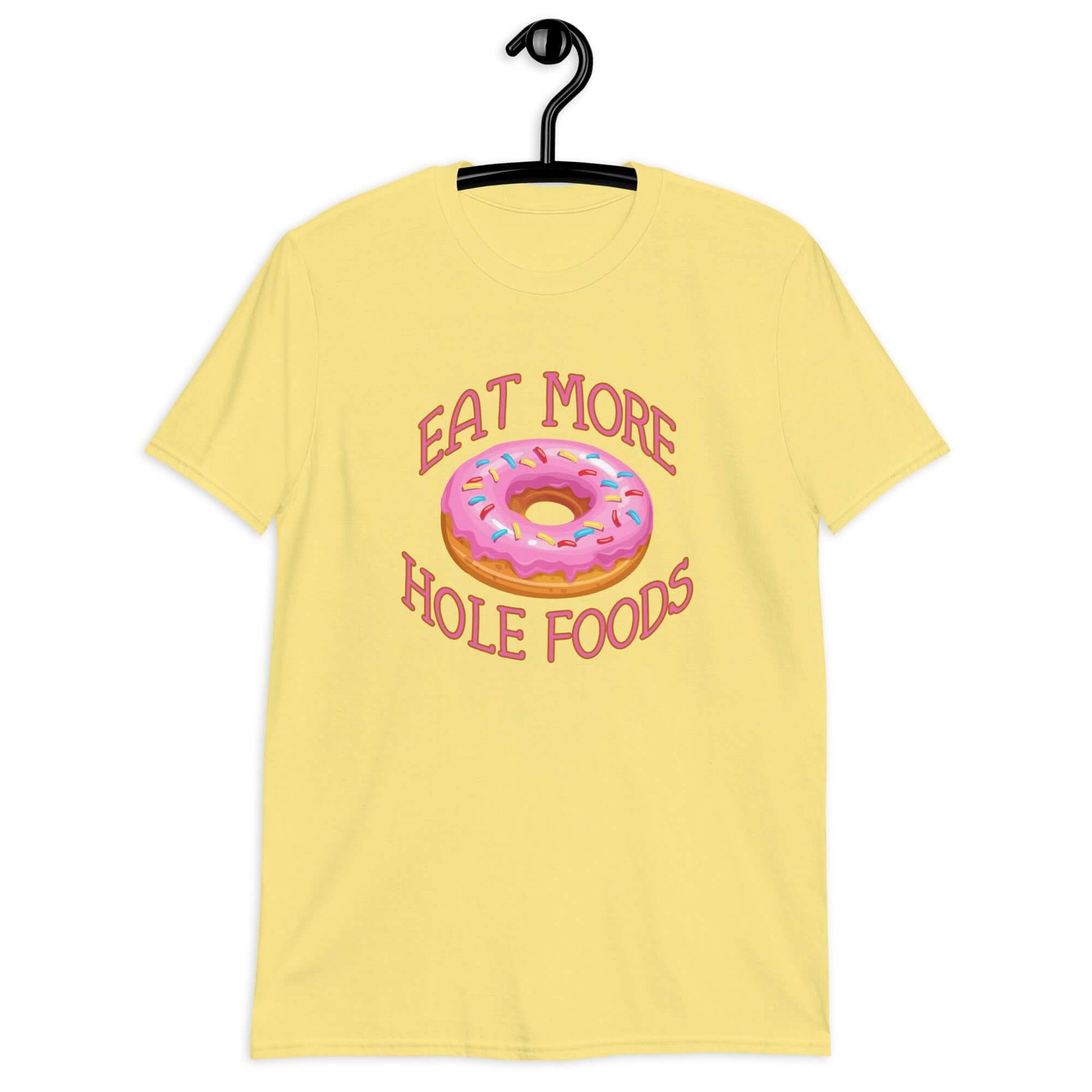 Cornsilk yellow t-shirt that has an image of a donut with pink icing and sprinkles and Eat more hole foods printed on the front.