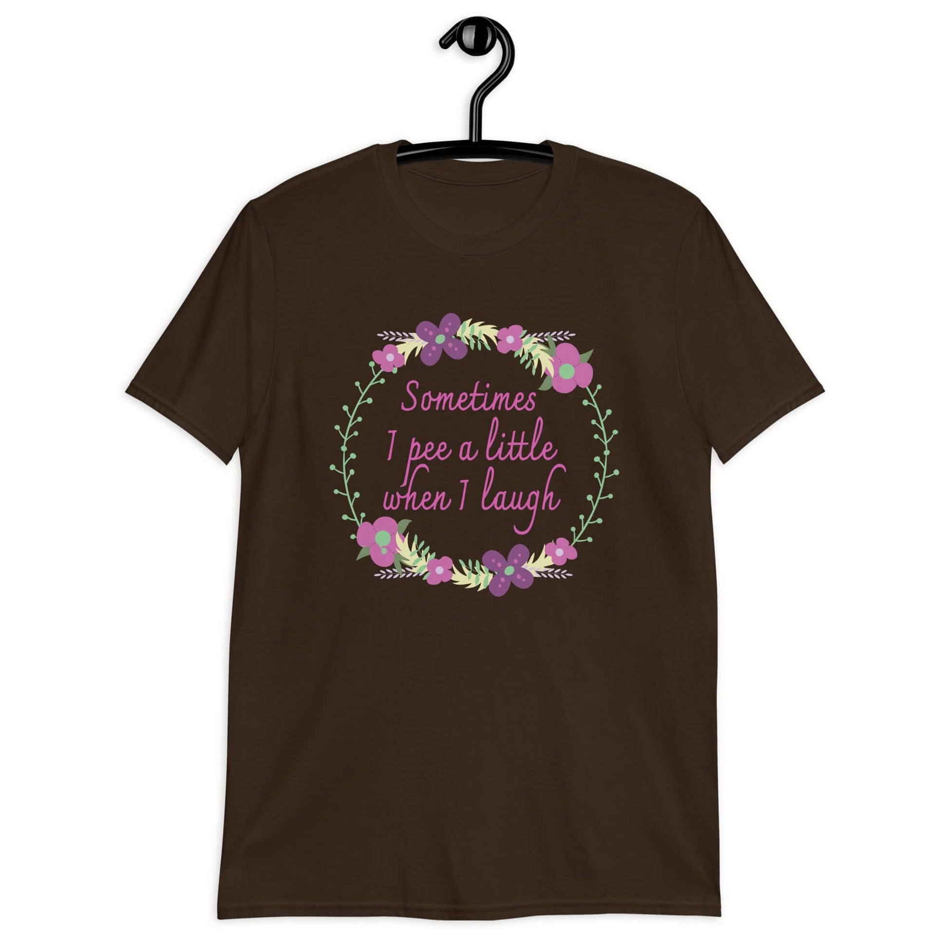Dark chocolate brown t-shirt that has a minimalistic style line drawing floral wreath with the phrase Sometimes I pee a little when I laugh printed in the center of the wreath. The graphics are printed on the front of the shirt.