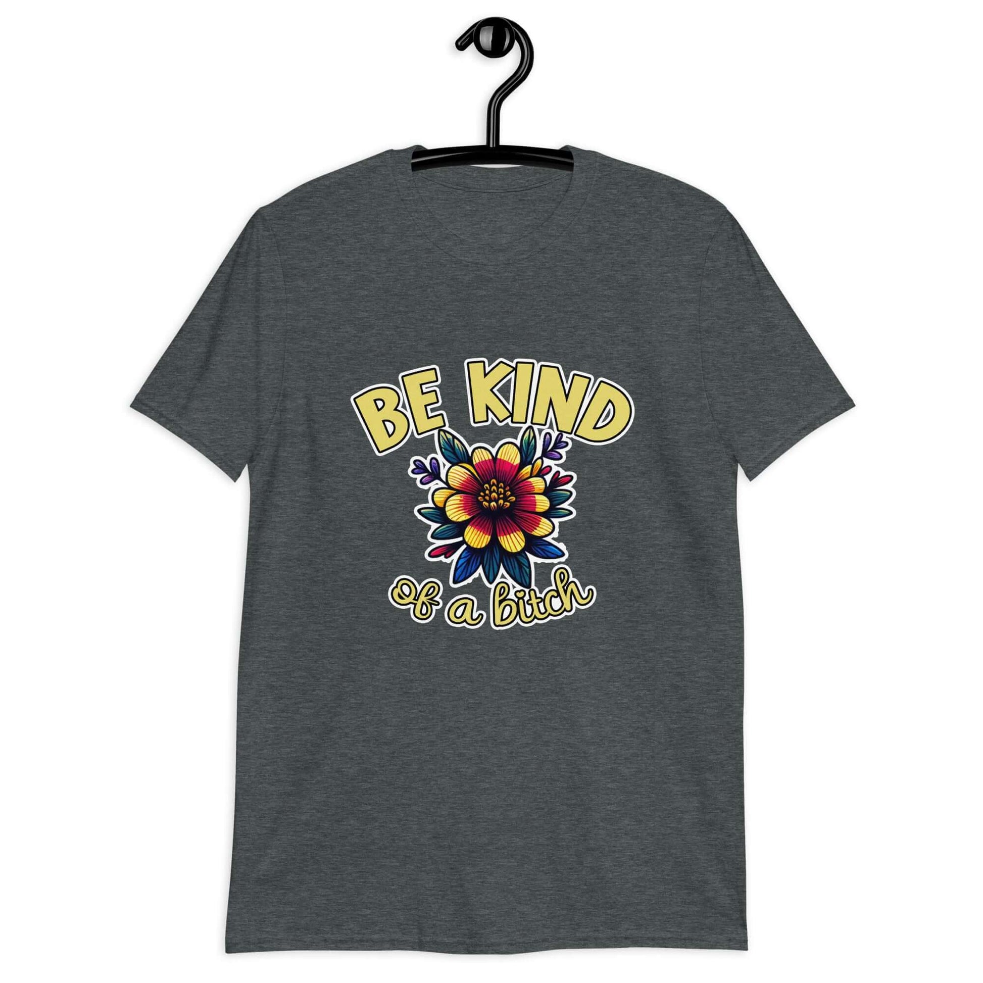 Dark heather grey t-shirt with an image of a flower and the words Be kind above the flower in yellow bold block font. The words Of a bitch are smaller in script font under the flower. The design is printed on the front of the shirt.