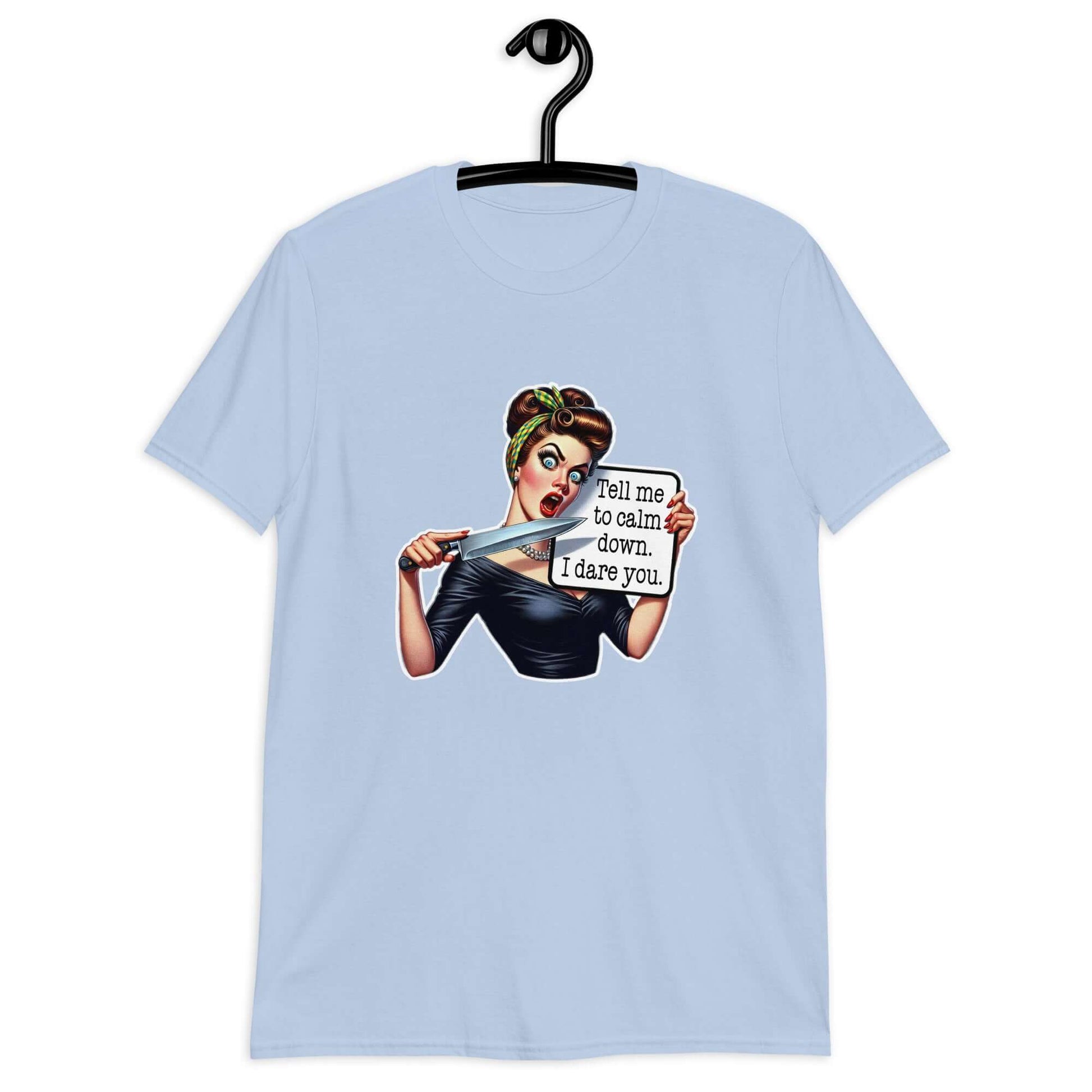 Light blue t-shirt displayed on a hanger. The t-shirt has a graphic of an angry looking retro woman holding a knife and a sign. The sign says Tell me to calm down I dare you. The graphic is printed on the front of the shirt.