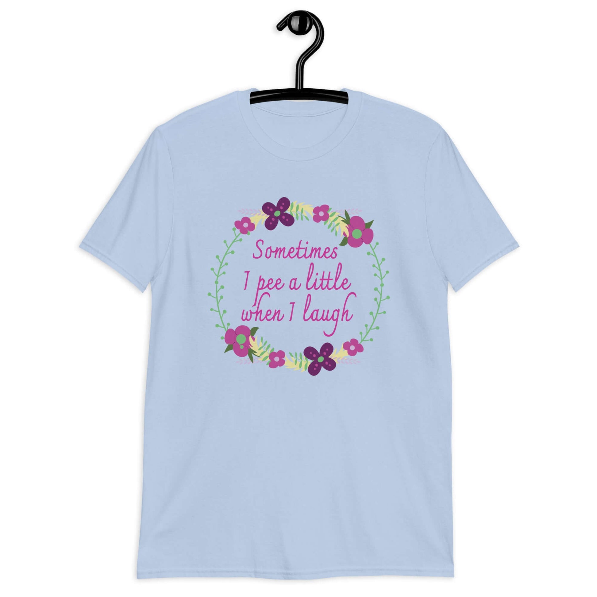 Light blue t-shirt that has a minimalistic style line drawing floral wreath with the phrase Sometimes I pee a little when I laugh printed in the center of the wreath. The graphics are printed on the front of the shirt.