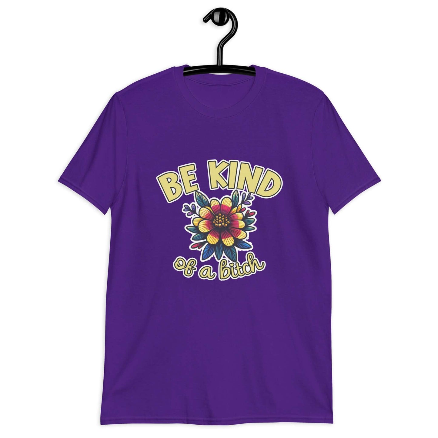 Purple t-shirt with an image of a flower and the words Be kind above the flower in yellow bold block font. The words Of a bitch are smaller in script font under the flower. The design is printed on the front of the shirt.