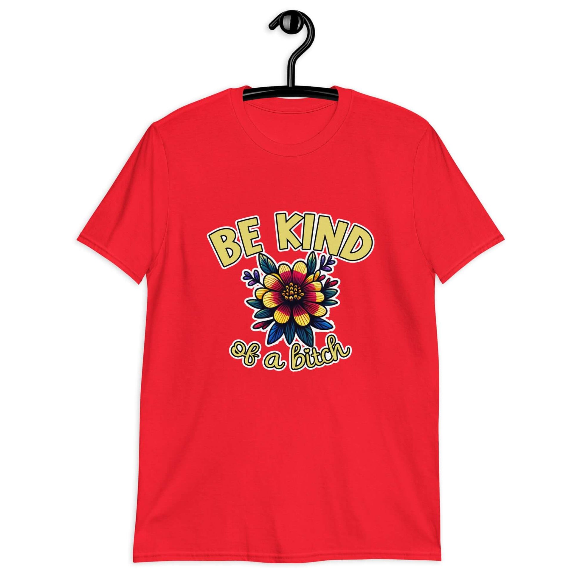 Red t-shirt with an image of a flower and the words Be kind above the flower in yellow bold block font. The words Of a bitch are smaller in script font under the flower. The design is printed on the front of the shirt.