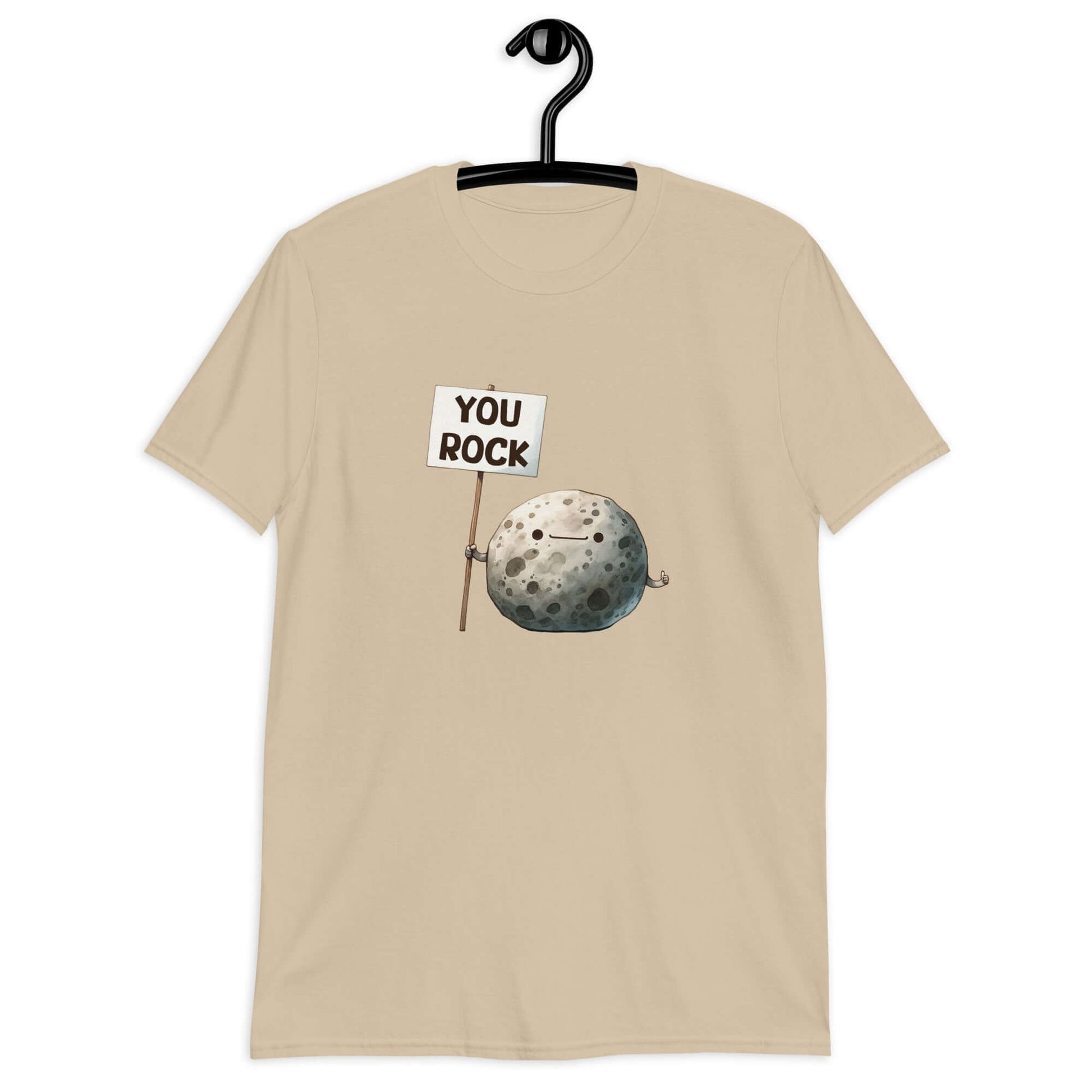 Sand color t-shirt that has an image of a grey rock that is holding a sign. The sign says You Rock. The image is printed on the front of the t-shirt..