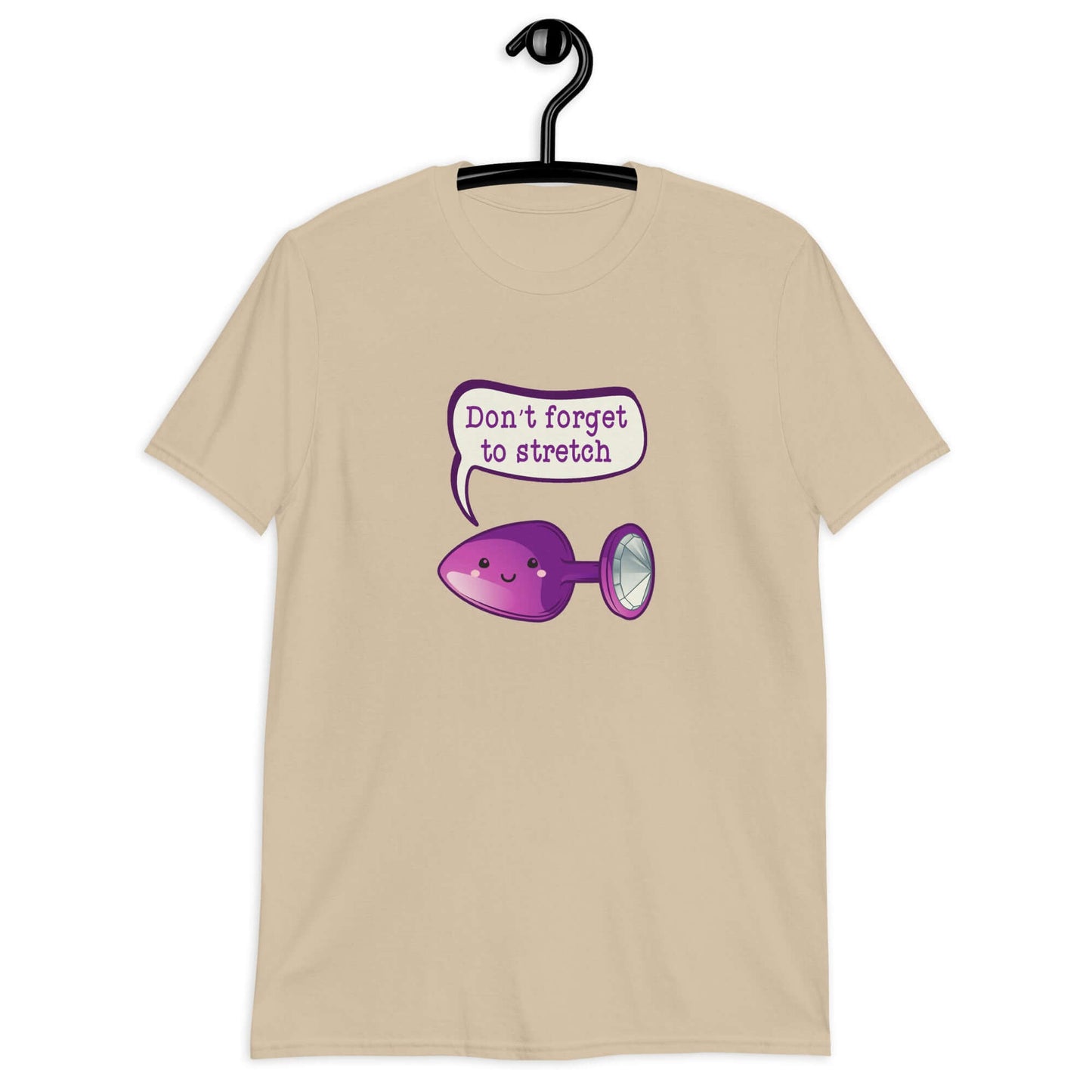 Sand color t-shirt that has image of a purple anal plug with a smile face with a speech bubble above with the words Don't forget to stretch. The graphics are printed on the front of the shirt.