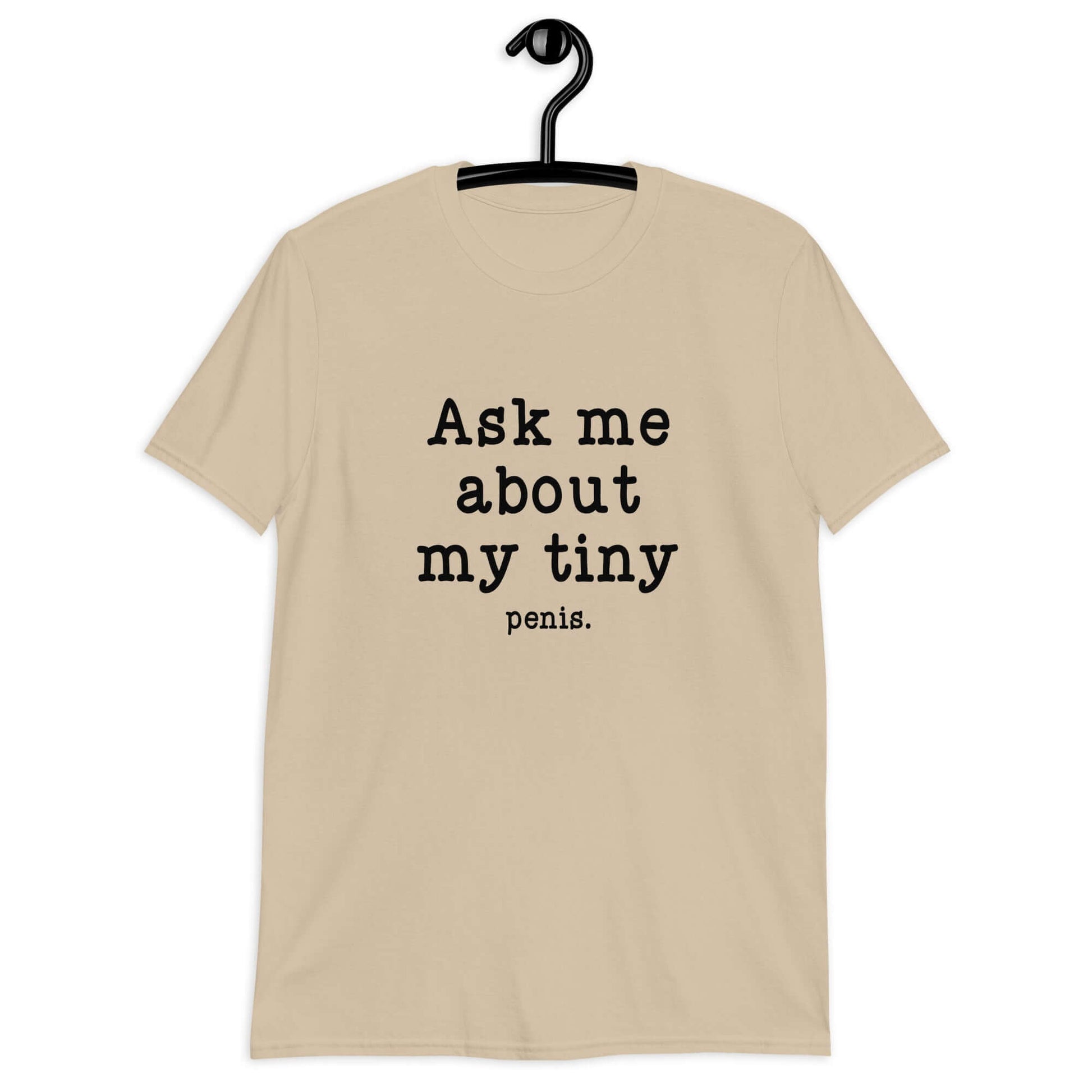 Sand color t-shirt with the phrase Ask me about my tiny penis printed on the front. The word tiny is much smaller than the rest of the text.