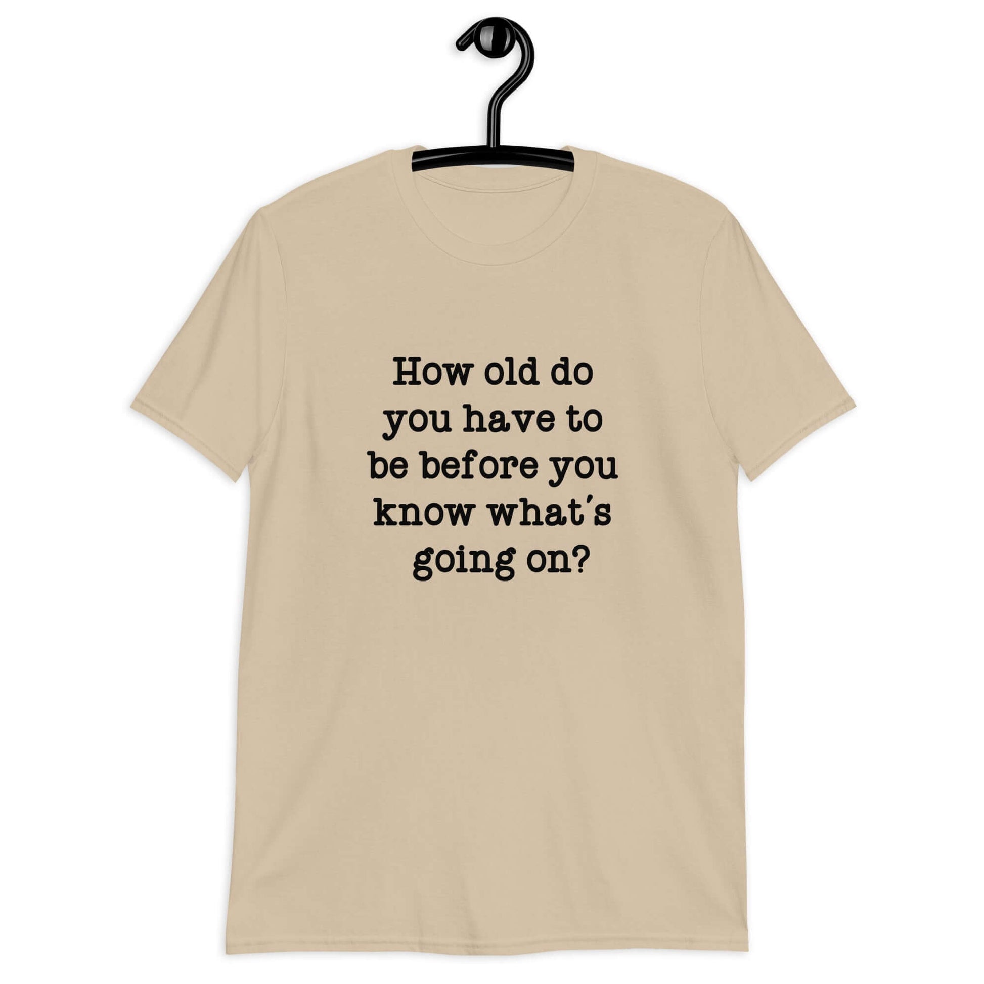 Sand color t-shirt with the phrase How old do you have to be before you know whats going on question mark printed on the front.