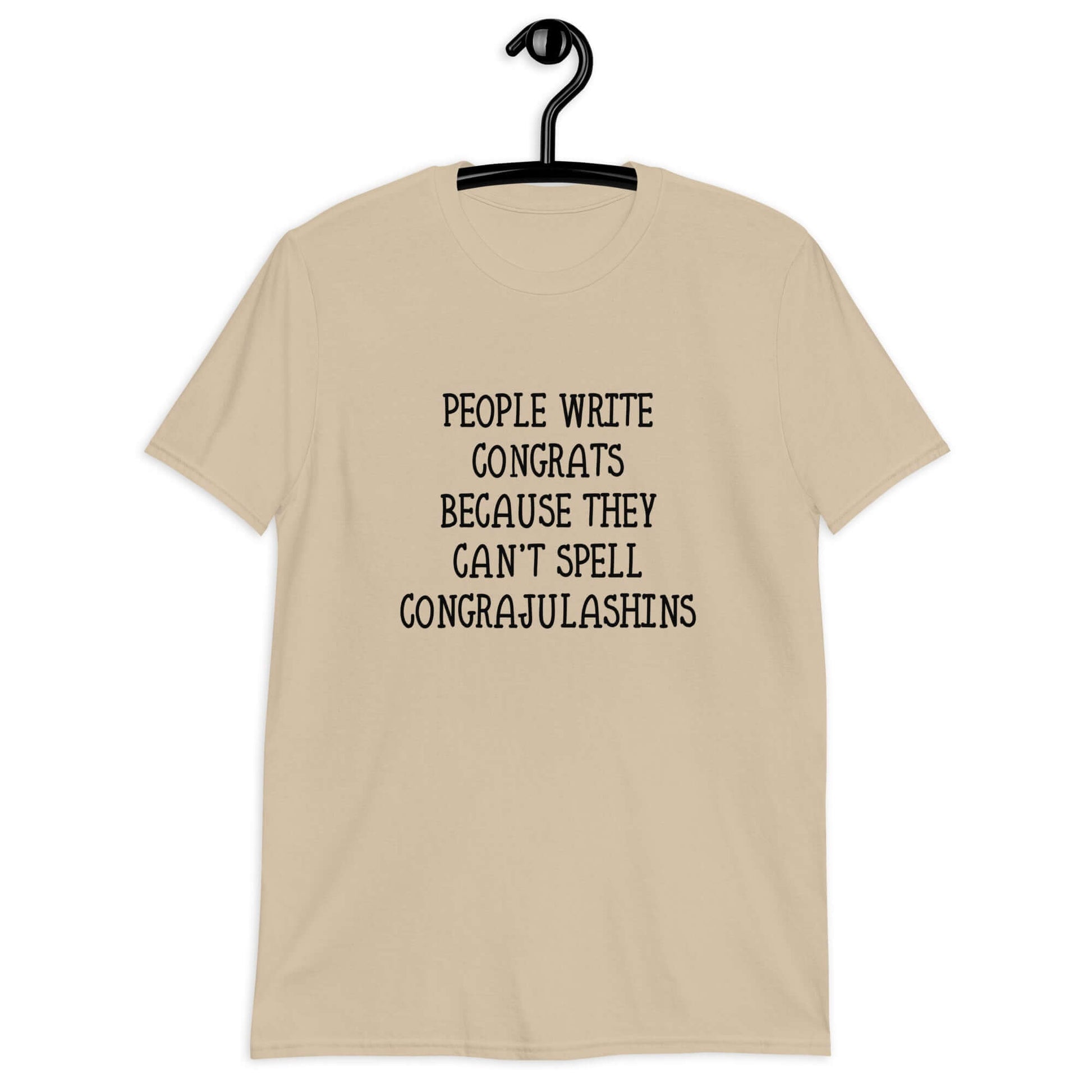 Sand t-shirt with the words People write congrats because they can't spell congratulations printed on the front. The word congratulations is intentionally misspelled.