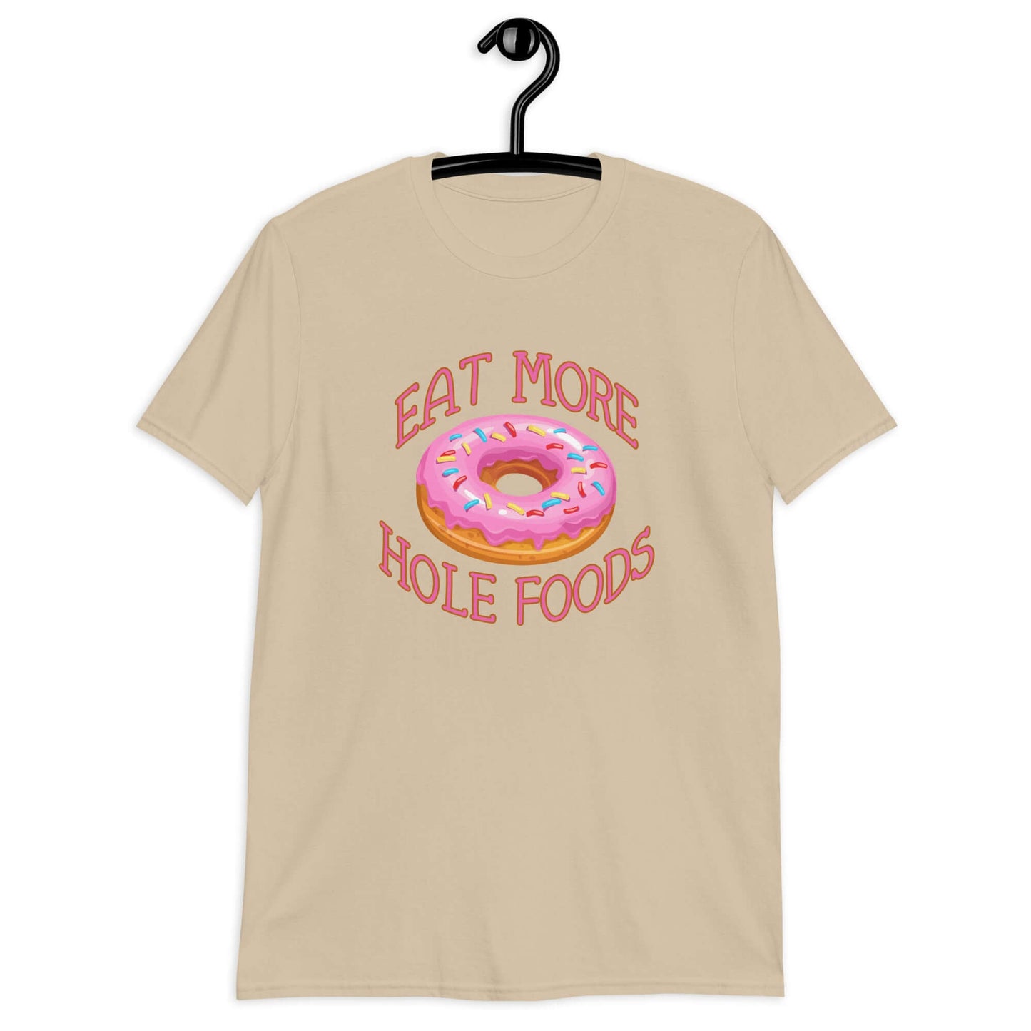 Sand color t-shirt that has an image of a donut with pink icing and sprinkles and Eat more hole foods printed on the front.