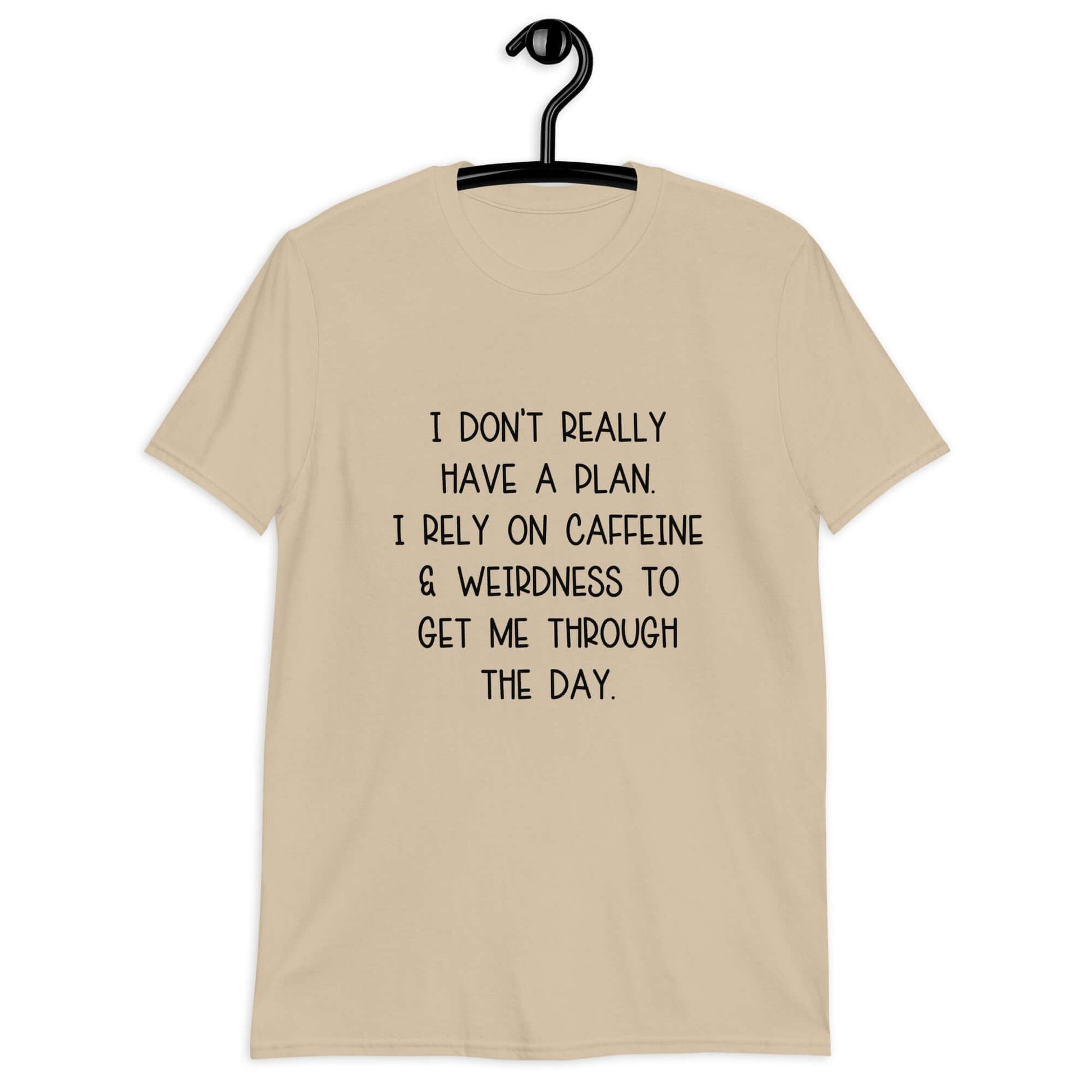 Sand color t-shirt with the phrase I don't really have a plan. I rely on caffeine & weirdness to get me through the day printed on the front.