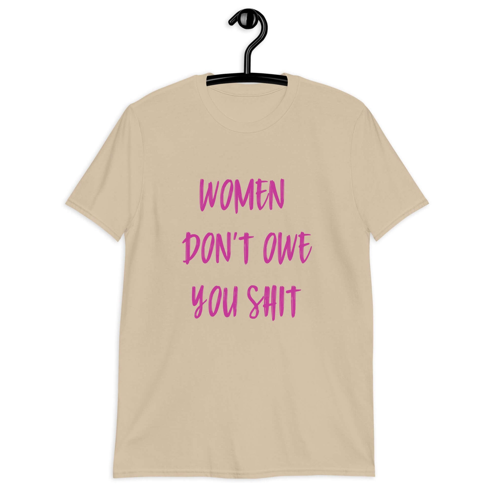 Sand color t-shirt with the words Women don't owe you shit printed on the front in pink.