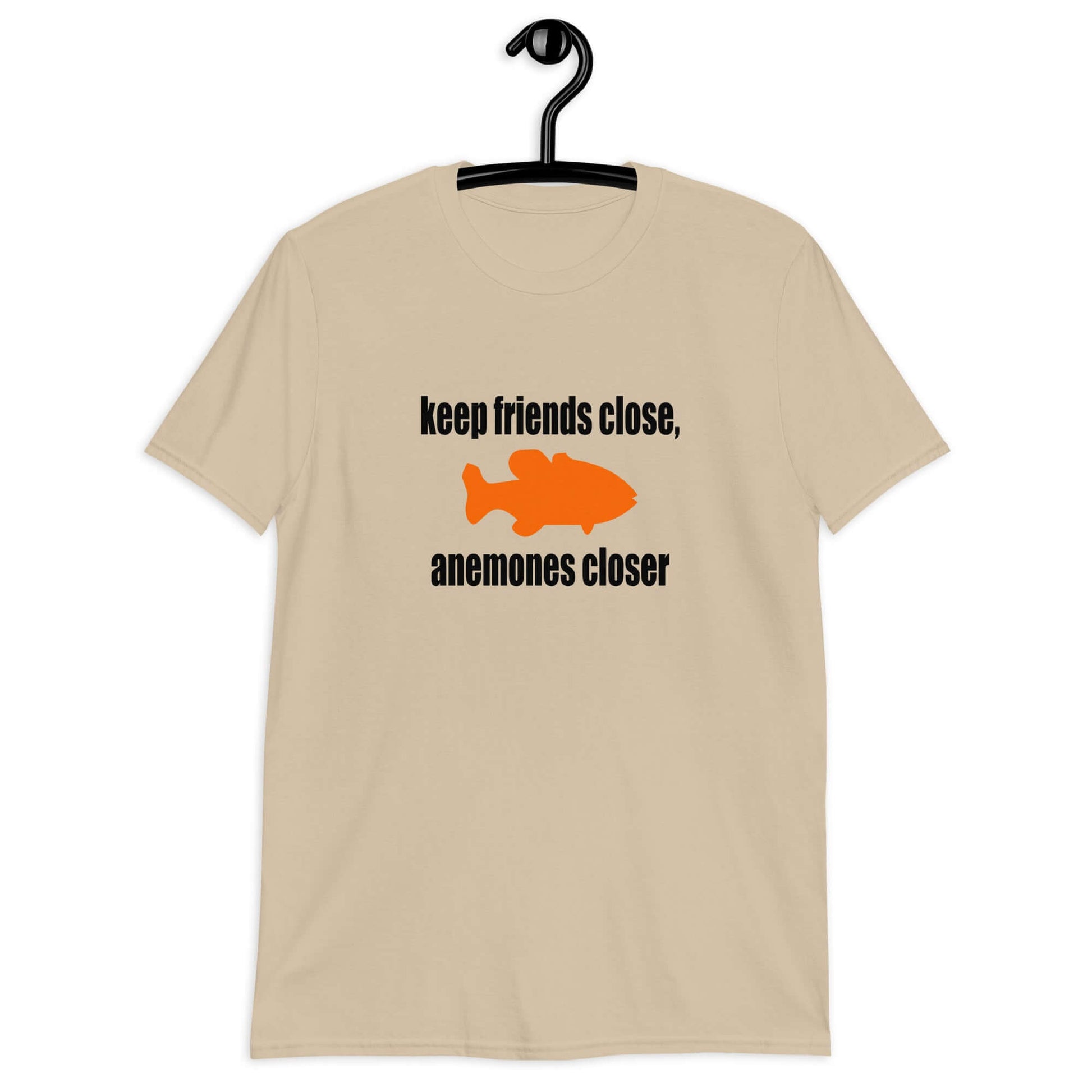 Sand color t-shirt with the pun phrase Keep friends close, anemones closer with an image of an orange fish.