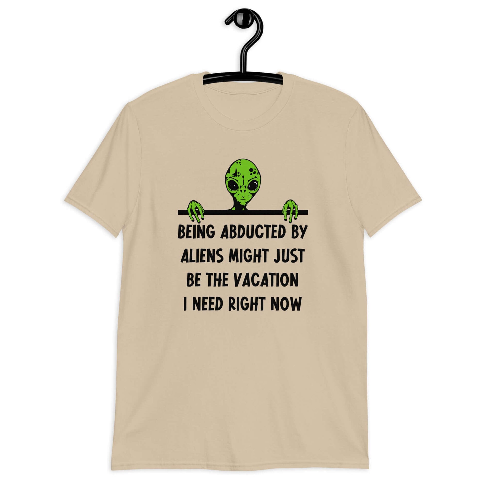 Sand color t-shirt with an image of a green alien and the phrase Being abducted by aliens might just be the vacation I need right now printed on the front of the shirt.