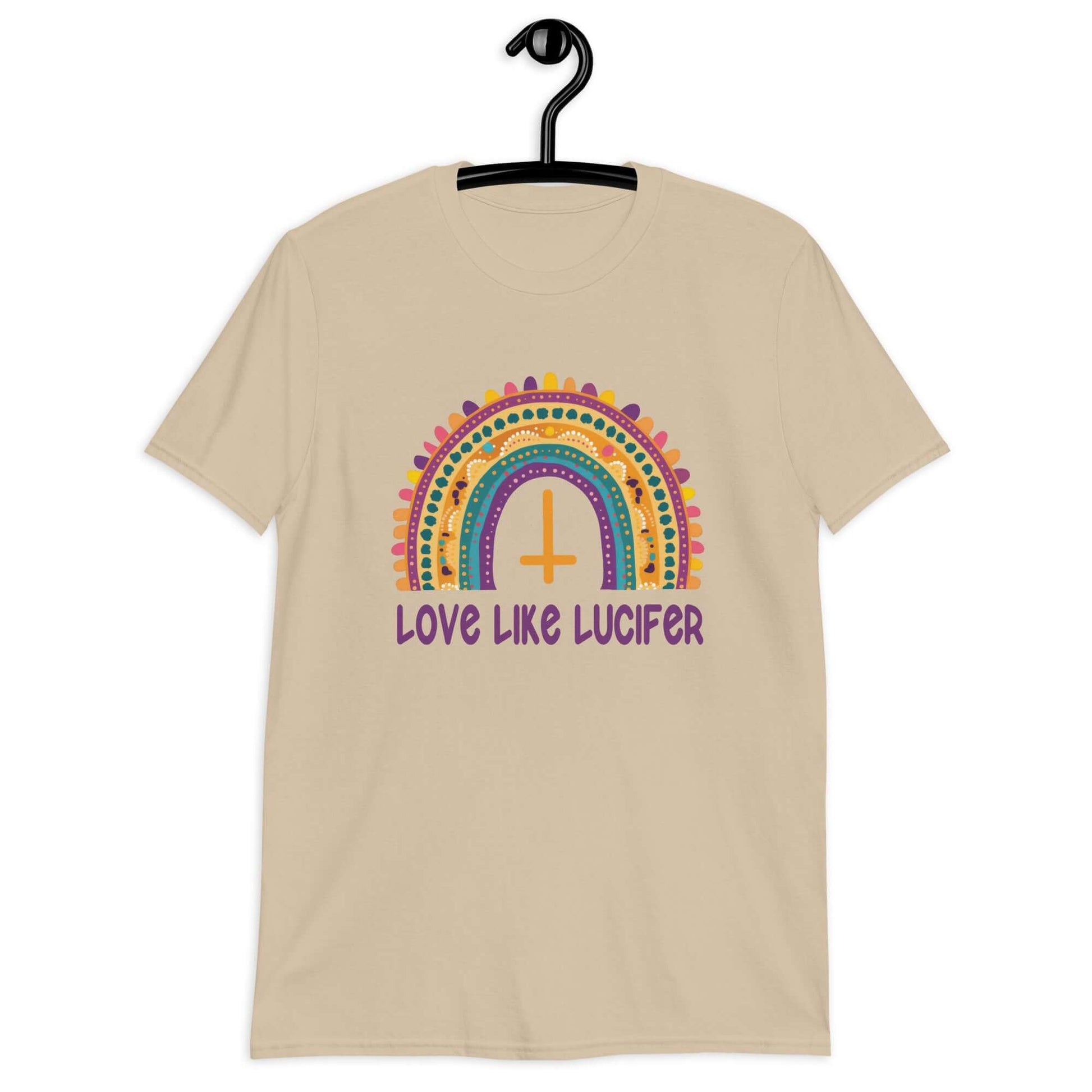 Sand color t-shirt with an image of a boho style rainbow. There is an upside down cross in the center arch of the rainbow and the phrase Love like Lucifer printed under. The graphics are printed on the front.