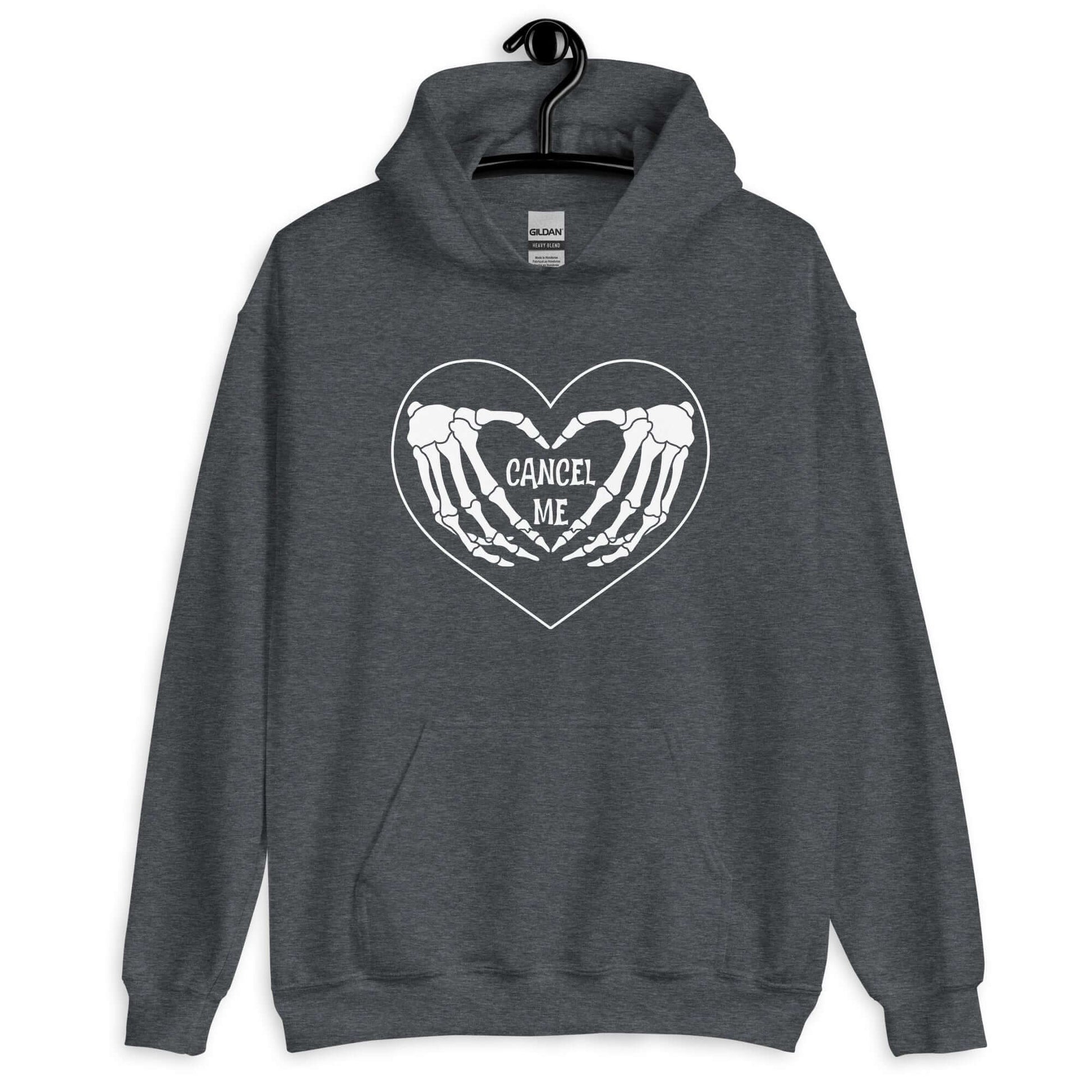 Dark heather grey hoodie sweatshirt with a black heart and skeleton hands making a heart shape printed on the front. The words Cancel Me are inside of the heart.