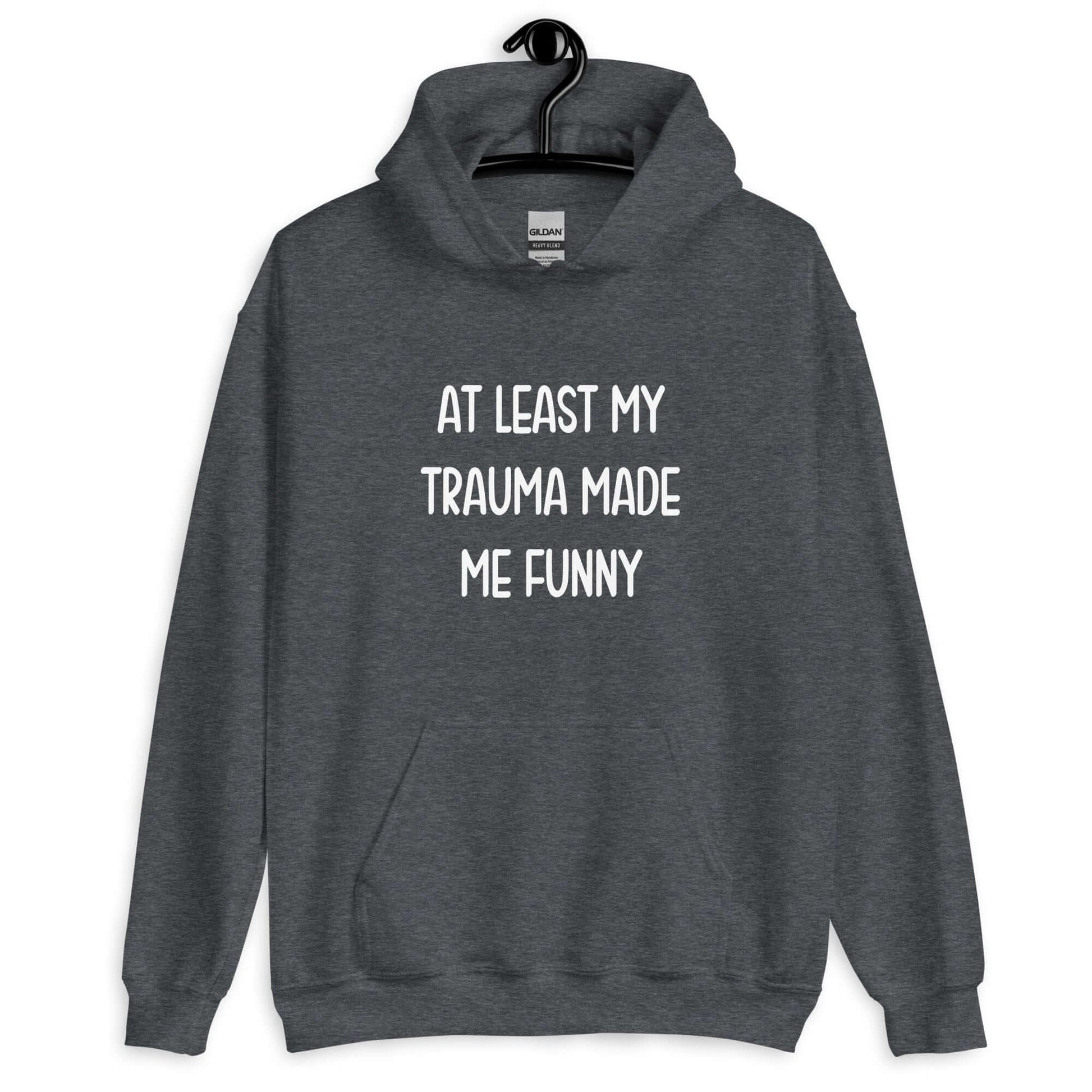 Dark heather grey hoodie sweatshirt with the words At least my trauma made me funny printed on the front.
