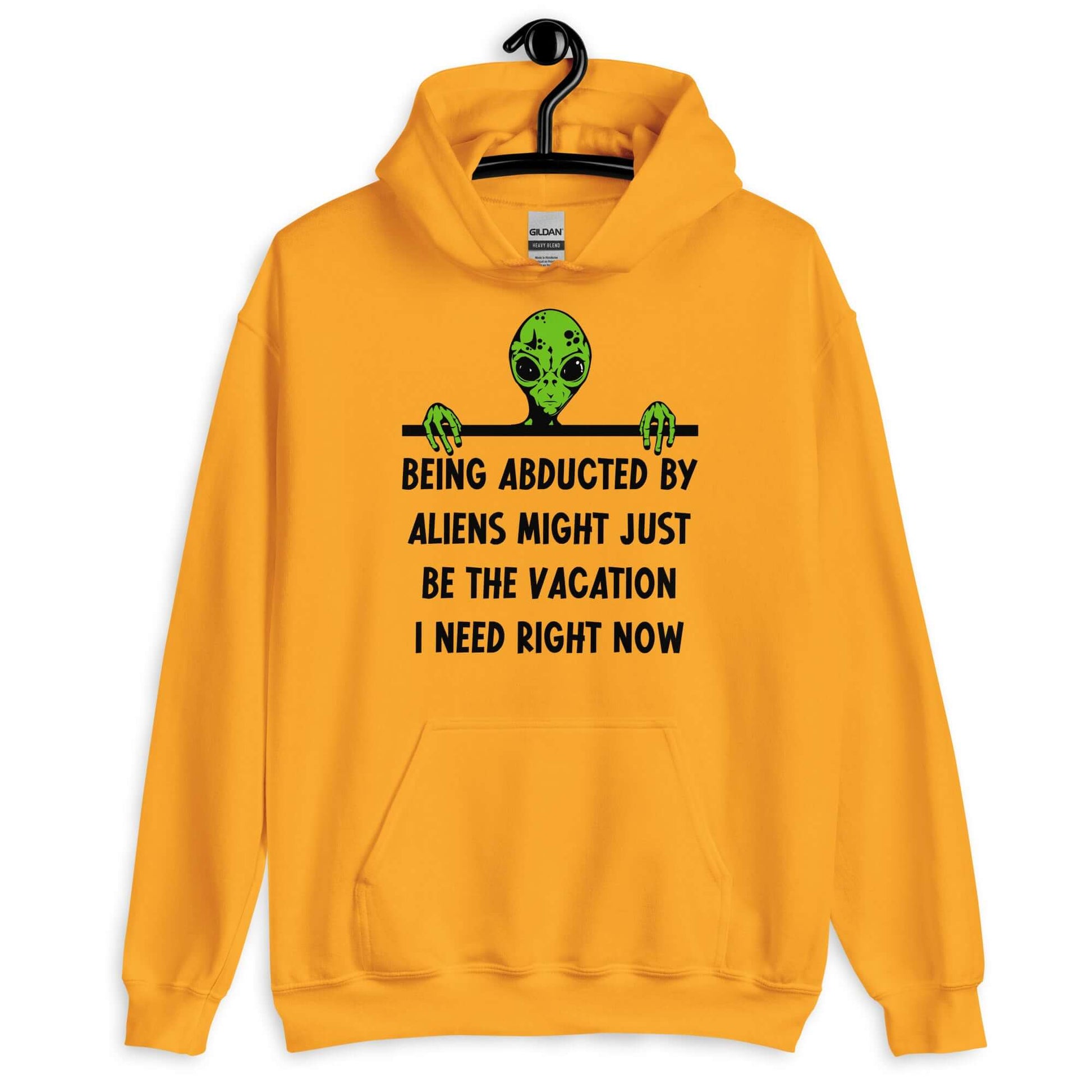 Golden yellow hoodie with an image of a green alien and the phrase Being abducted by aliens might just be the vacation I need right now printed on the front of the sweatshirt.