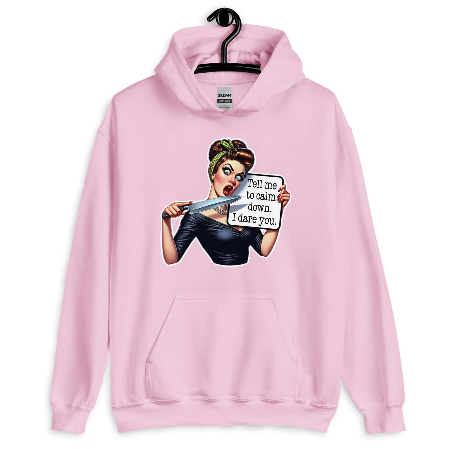 Light pink hooded sweatshirt displayed on a hanger. The sweatshirt has a graphic of an angry looking retro woman holding a knife and a sign. The sign says Tell me to calm down I dare you. The graphic is printed on the front of the hoodie.