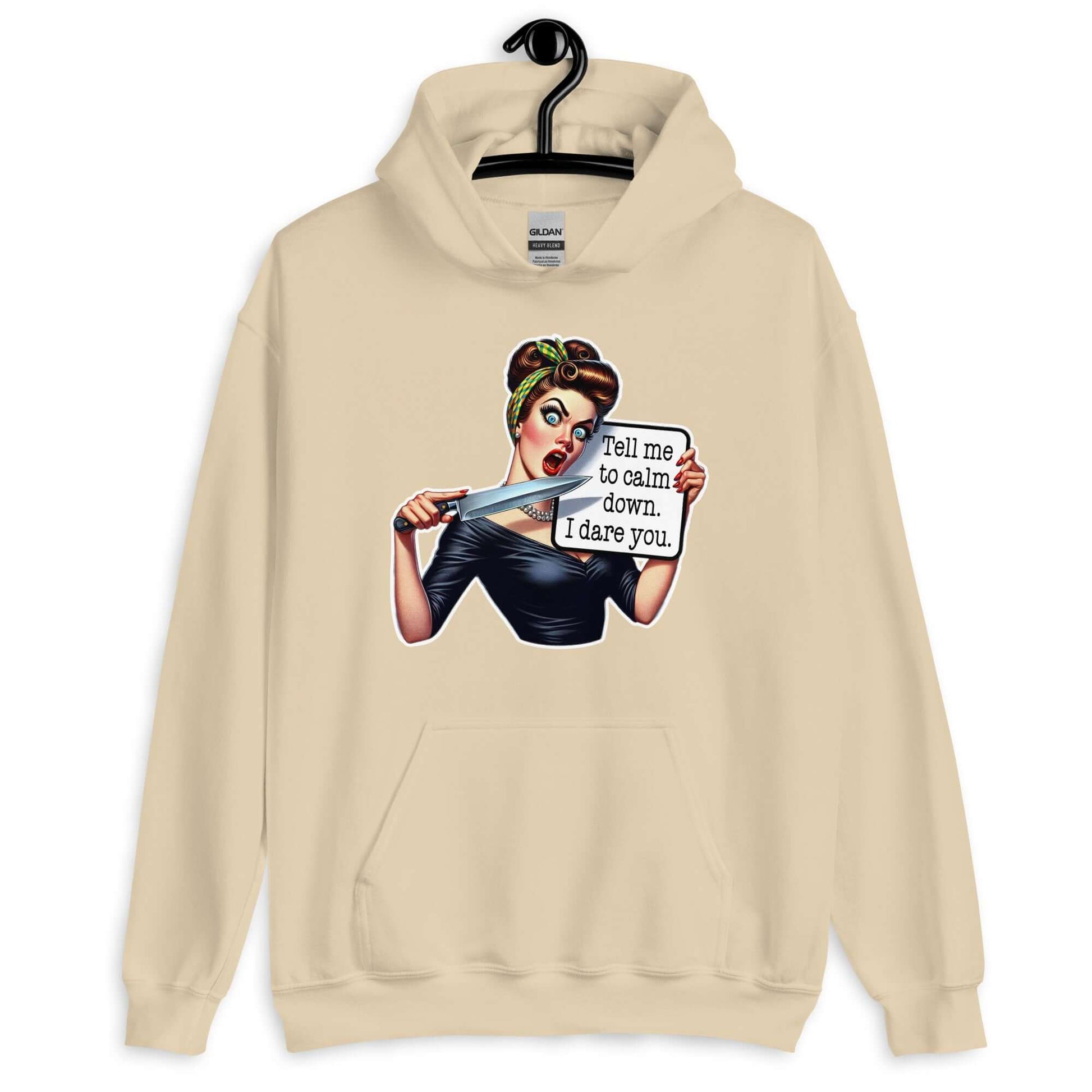 Sand hoodie sweatshirt displayed on a hanger. The sweatshirt has a graphic of an angry looking retro woman holding a knife and a sign. The sign says Tell me to calm down I dare you. The graphic is printed on the front of the hoodie.