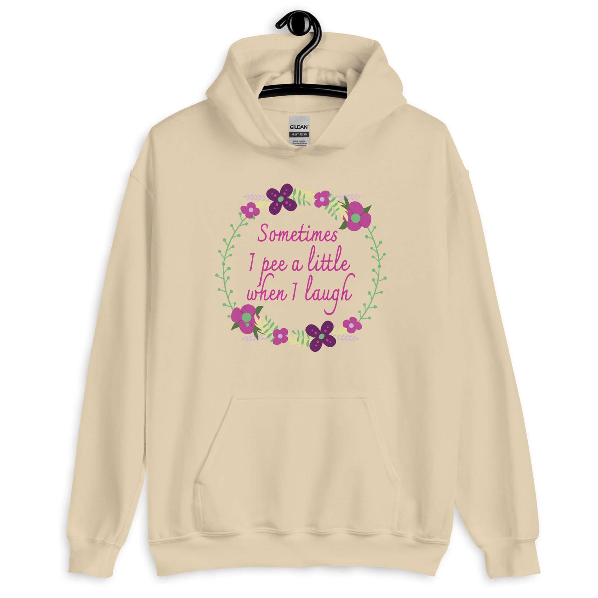 Sand hoodie sweatshirt that has a minimalistic style line drawing floral wreath with the phrase Sometimes I pee a little when I laugh printed in the center of the wreath. The graphics are printed on the front of the hoodie.