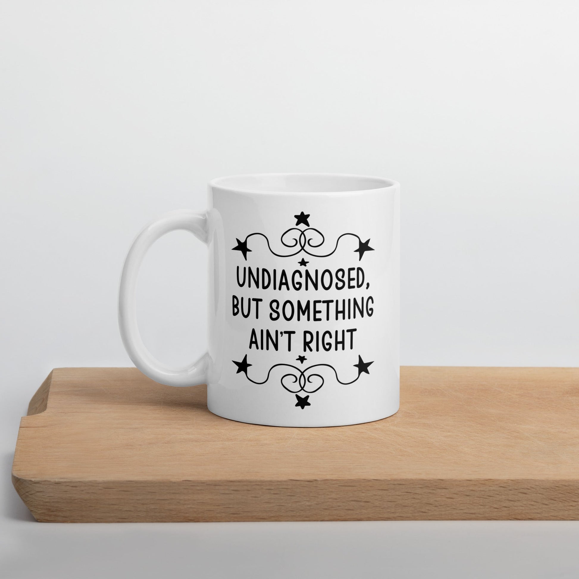 11 ounce white ceramic mug with the phrase Undiagnosed, but something ain't right printed on both sides.