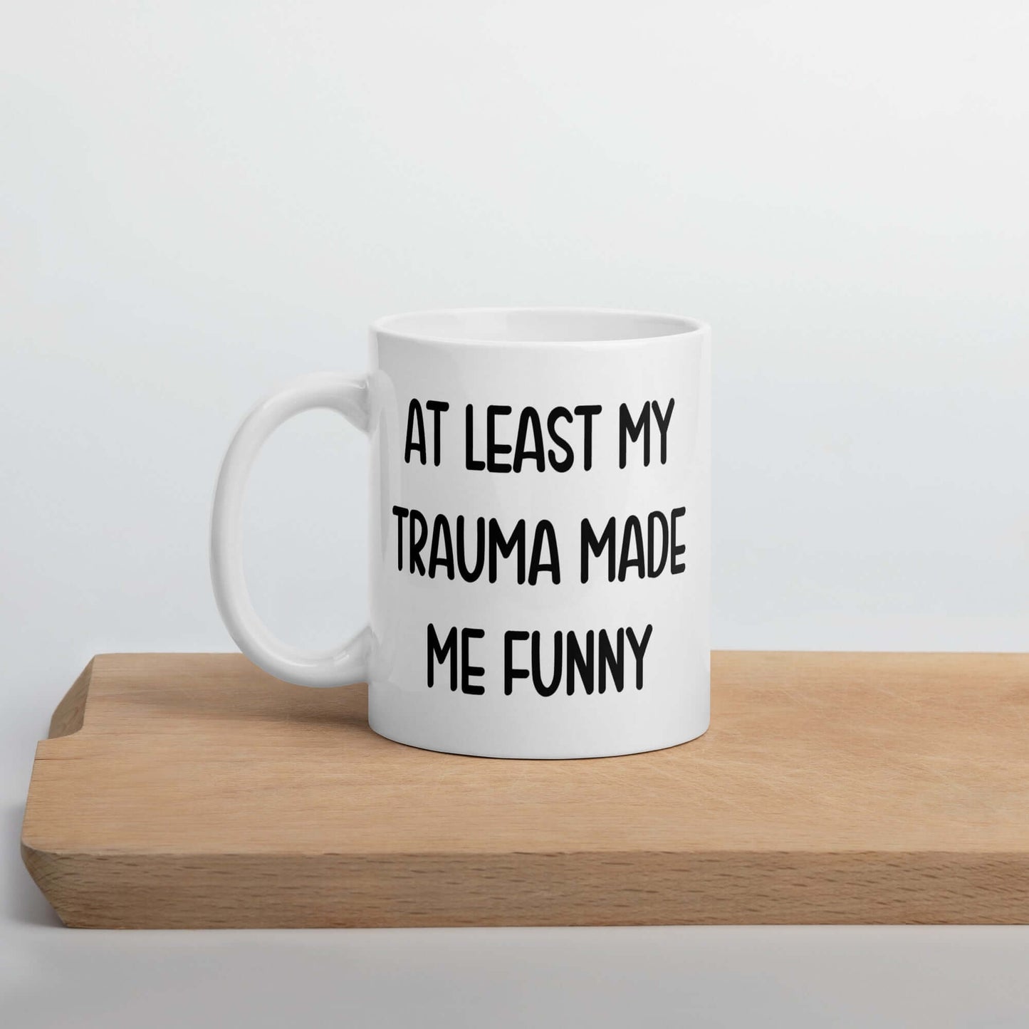 White ceramic mug with the words At least my trauma made me funny printed on both sides.