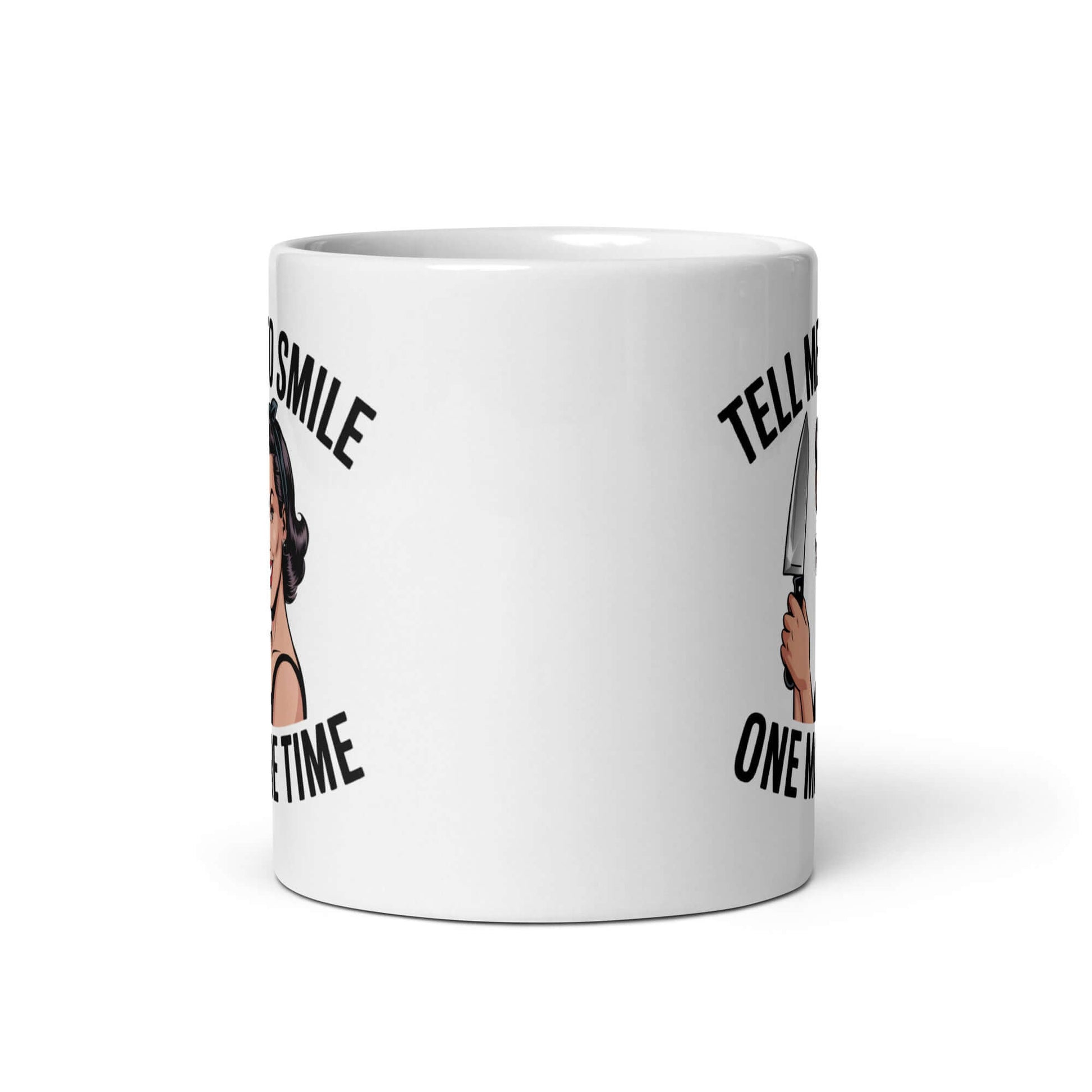 White ceramic mug with graphic of a woman holding a knife and the phrase 'Tell me to smile one more time'. 