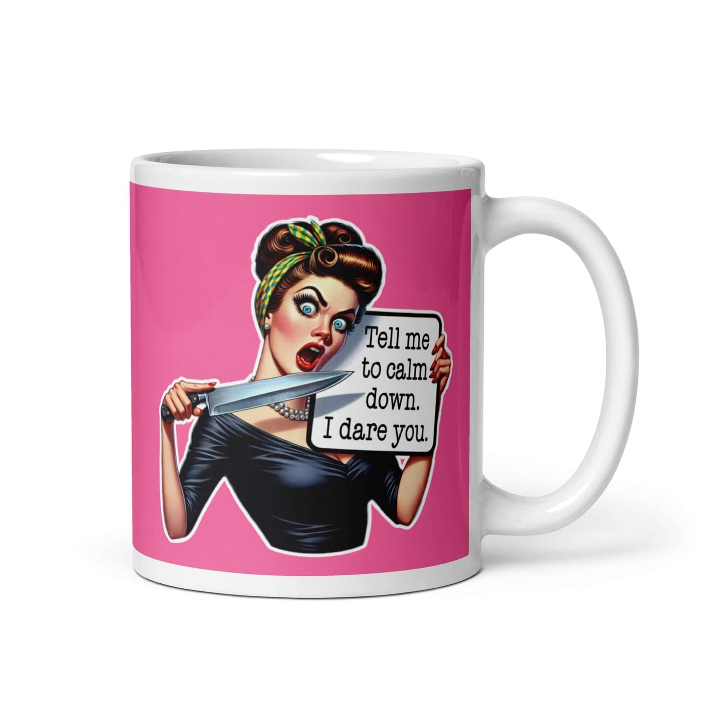 White ceramic coffee mug with pink color wrapped around. The mug has a graphic of an angry looking retro woman holding a knife and a sign. The sign says Tell me to calm down I dare you. The graphic is printed on both sides of the mug.