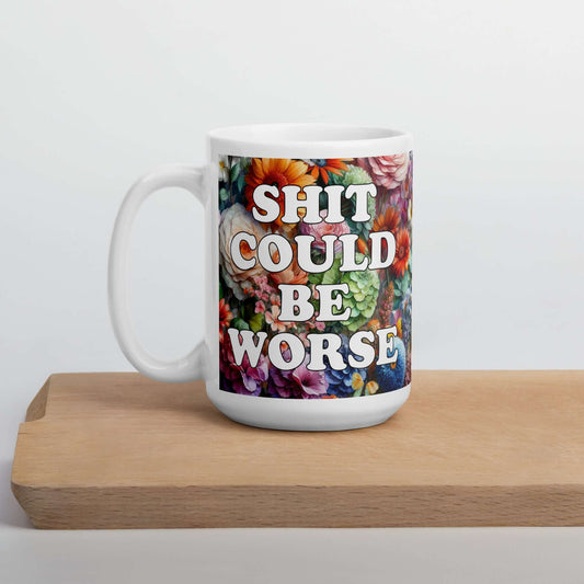 White ceramic mug floral background and the words Shit could be worse printed on both sides. 