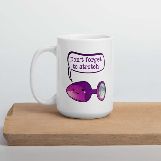 White ceramic mug that has image of a purple anal plug with a smile face with a speech bubble above with the words Don't forget to stretch. The graphics are printed on both sides of the mug.