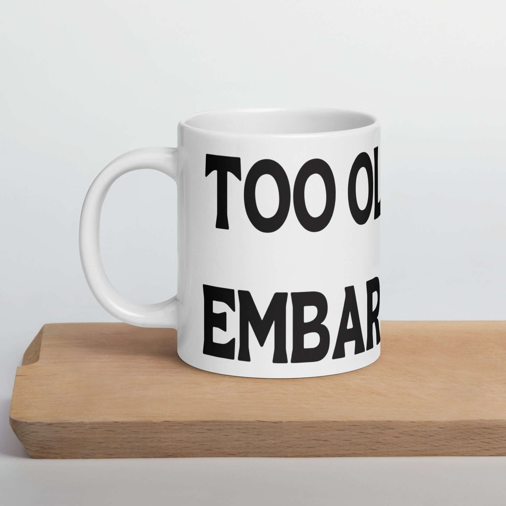 White ceramic mug with the words Too old to be embarrassed printed on it. 