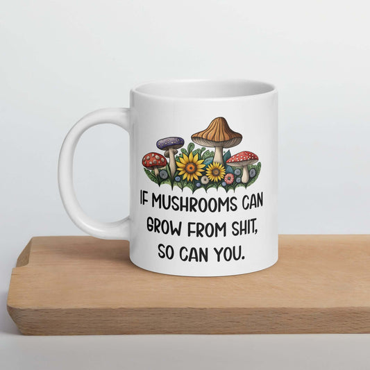 White ceramic mug with images of mushrooms and the phrase If mushrooms can grow from shit so can you printed on both sides of the mug.