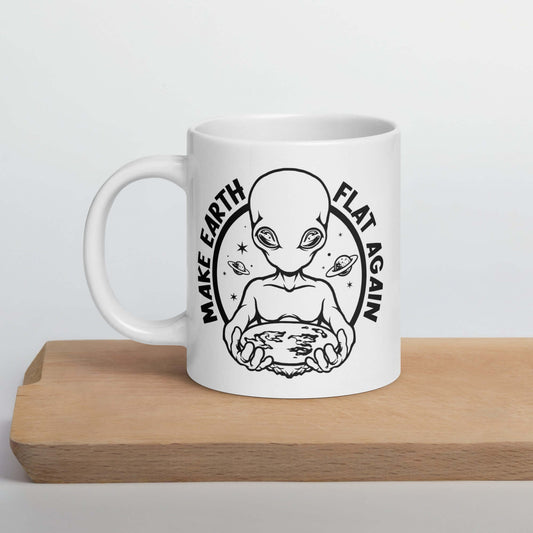 White ceramic coffee mug with an image of an alien holding flat earth and the phrase Make earth flat again printed on both sides.