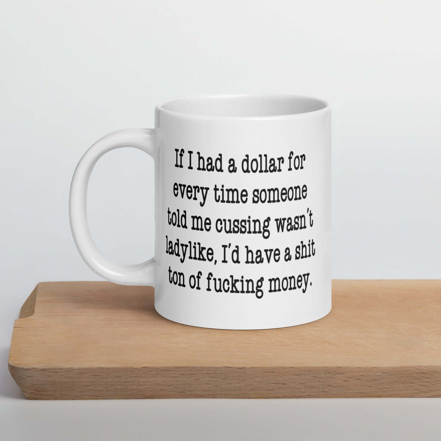 White ceramic mug with the phrase If I had a dollar for every time someone told me cussing wasn't ladylike I'd have a shit ton of fucking money printed on both sides of the mug.